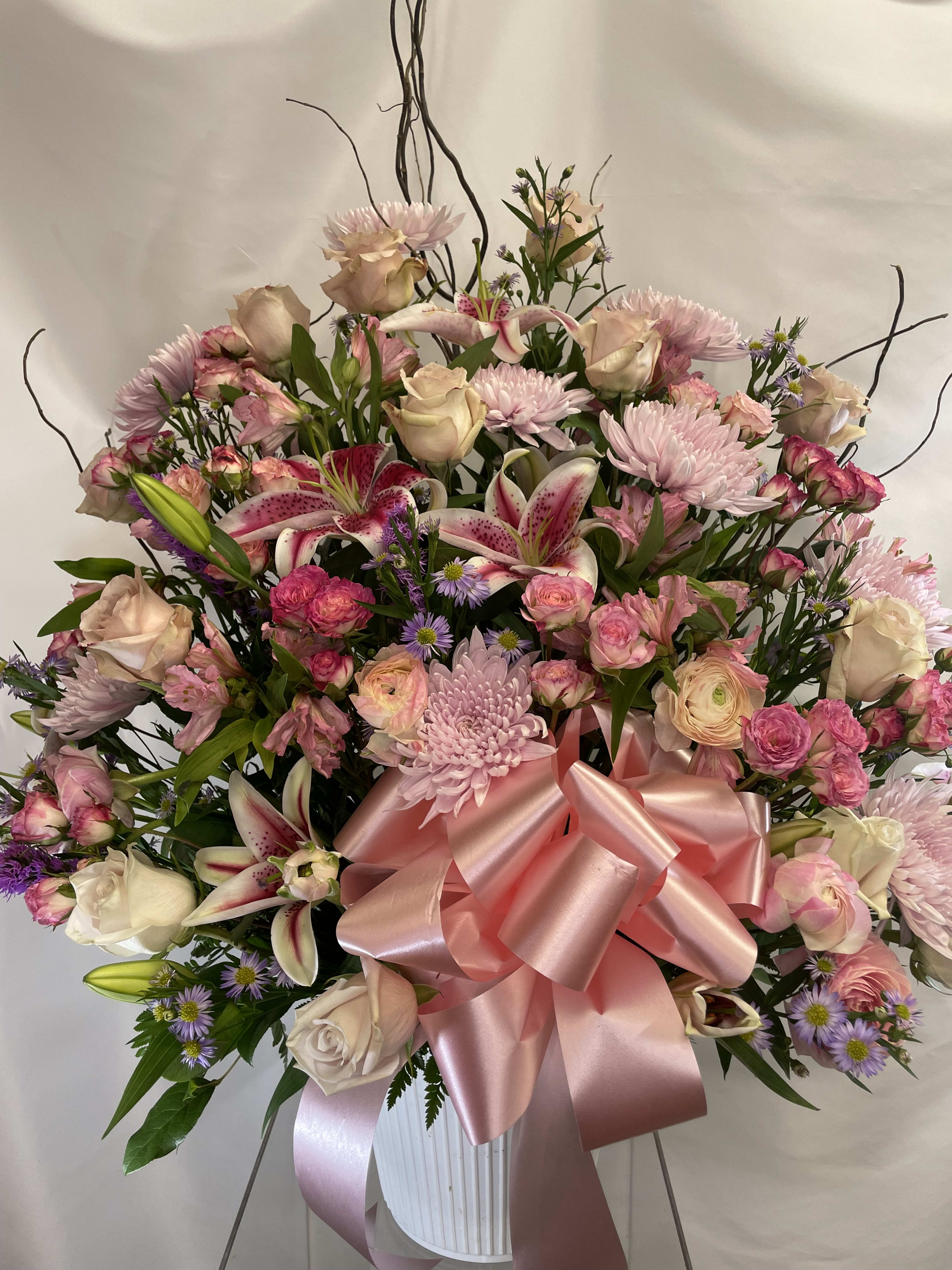 Large pink and white floral arrangement with a satin bow in a white vase