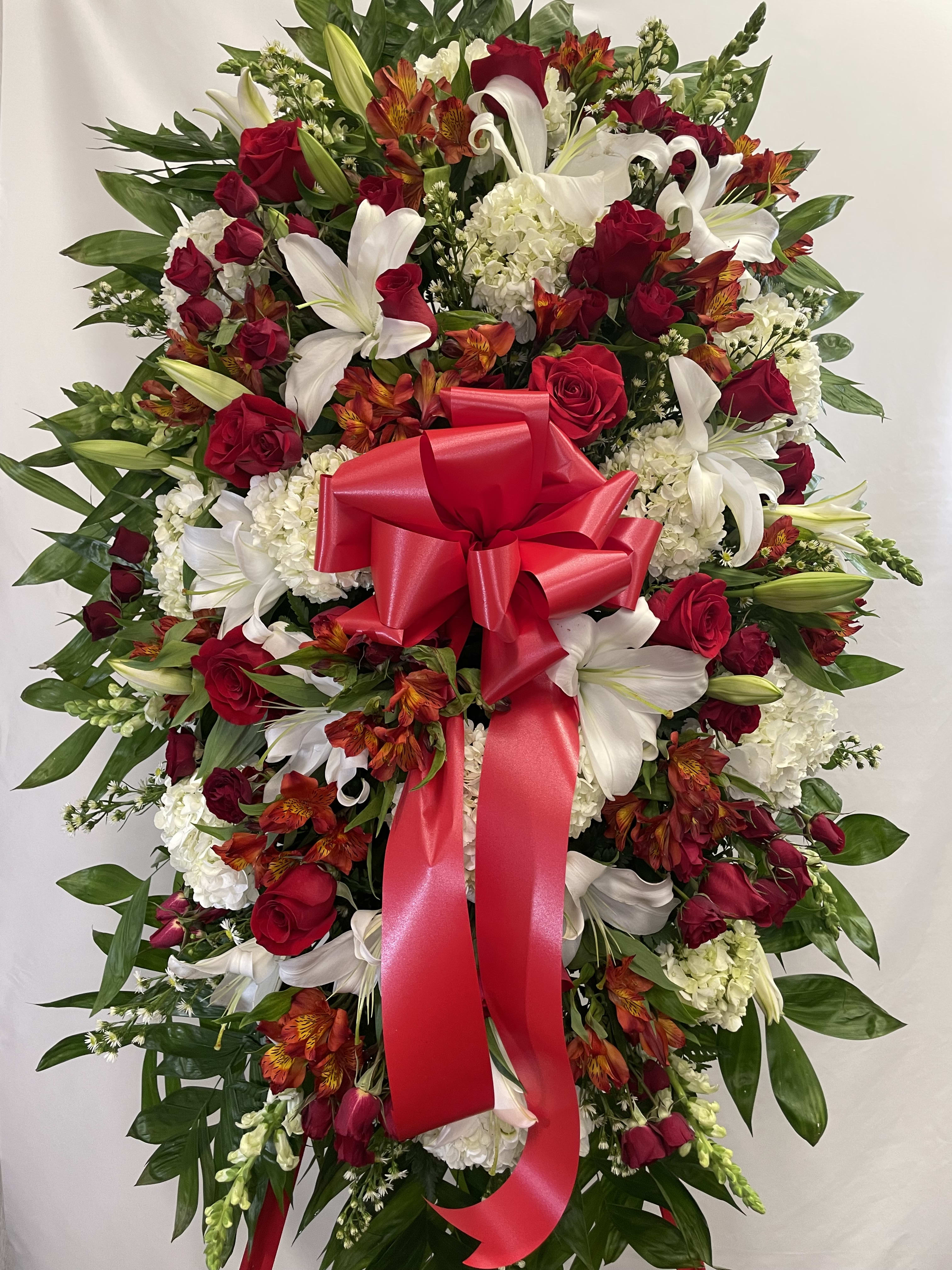 Standing floral spray with red roses, white lilies, and a red ribbon bow