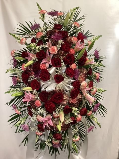 Large standing floral spray with red roses, pink lilies, and a white ribbon bow