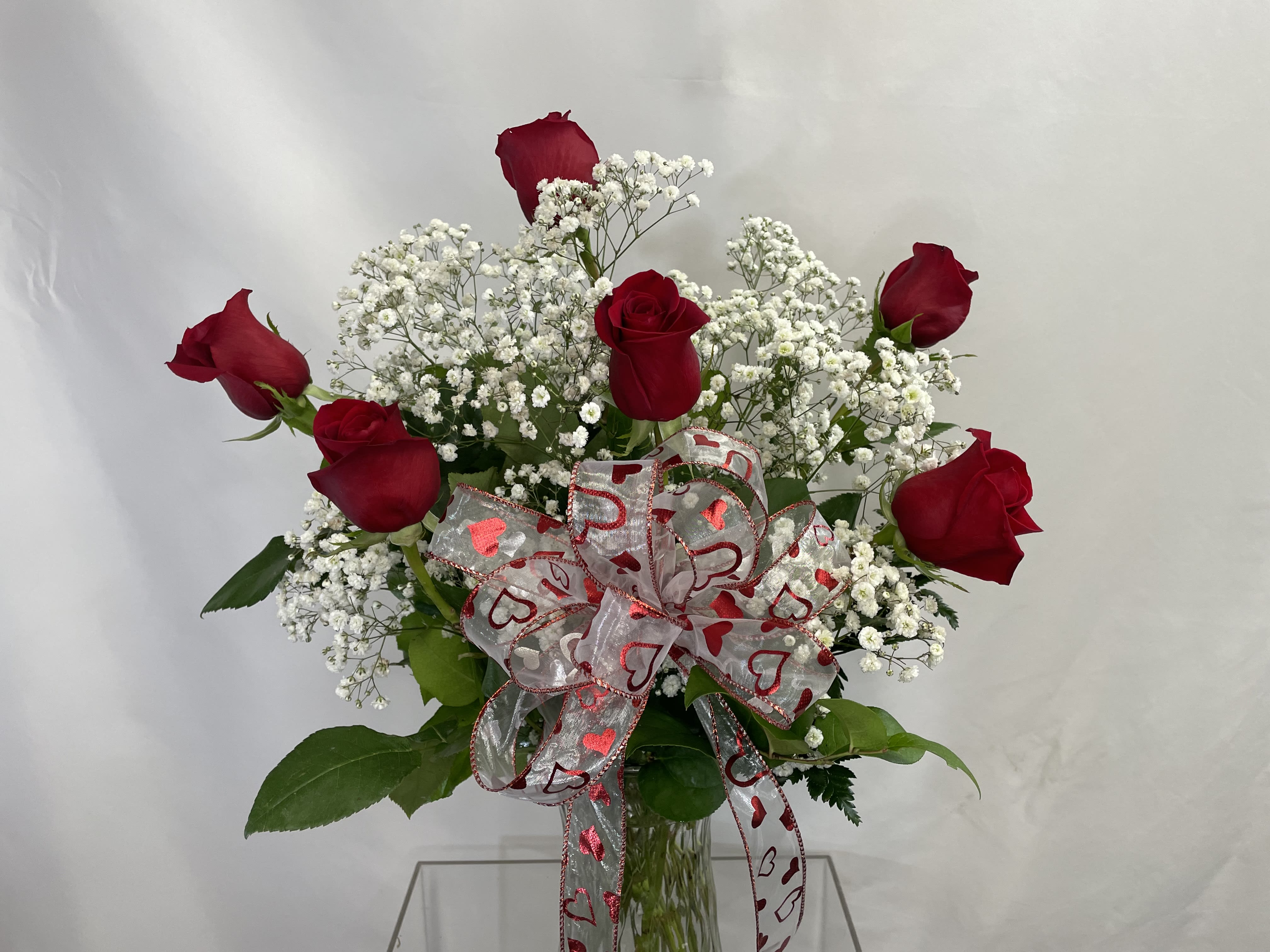Red roses with white baby's breath in a glass vase, tied with a heart ribbon