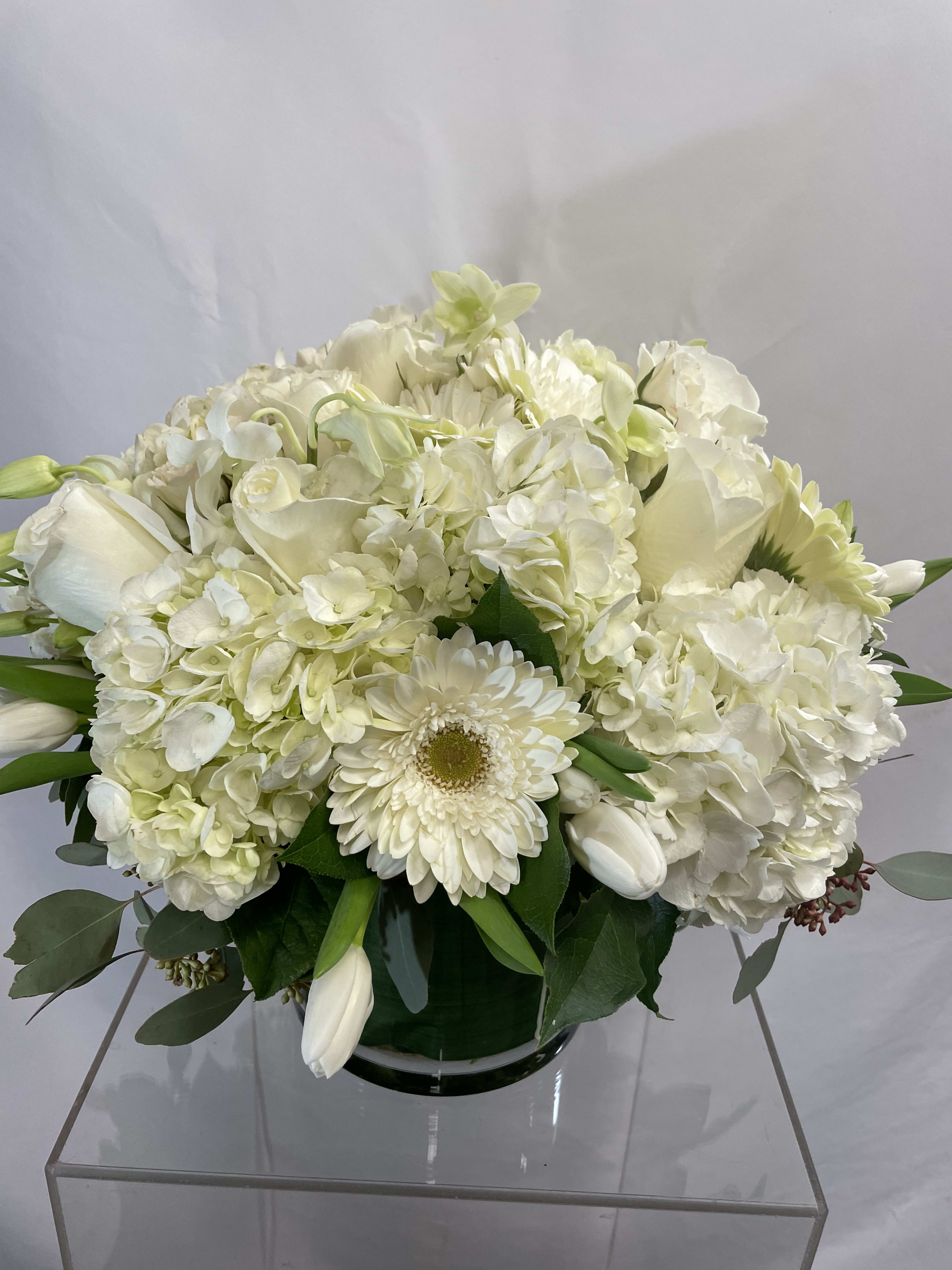 White floral arrangement in a glass vase with hydrangeas, roses, and daisies