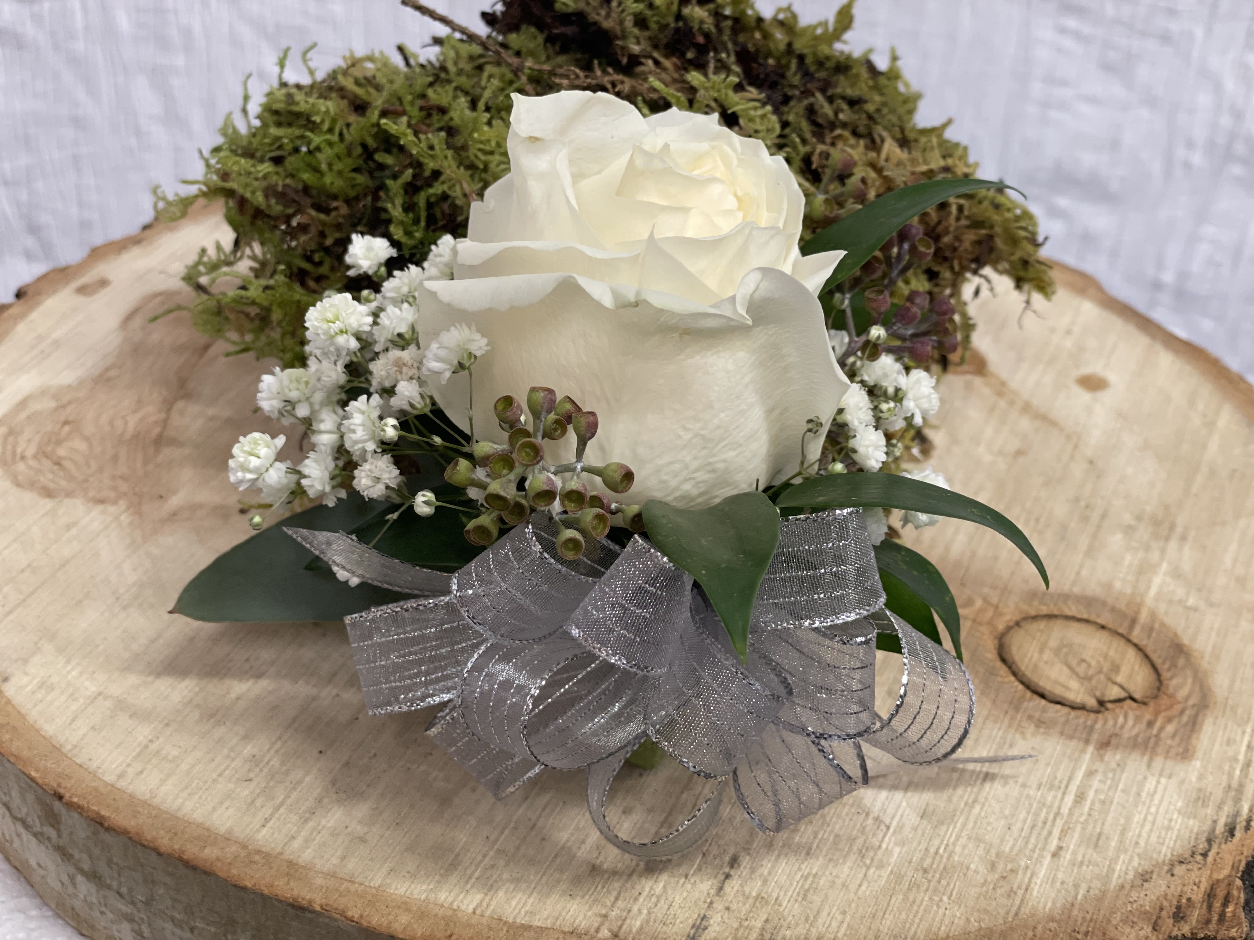 White rose arrangement with baby's breath and silver ribbon on a wood slice