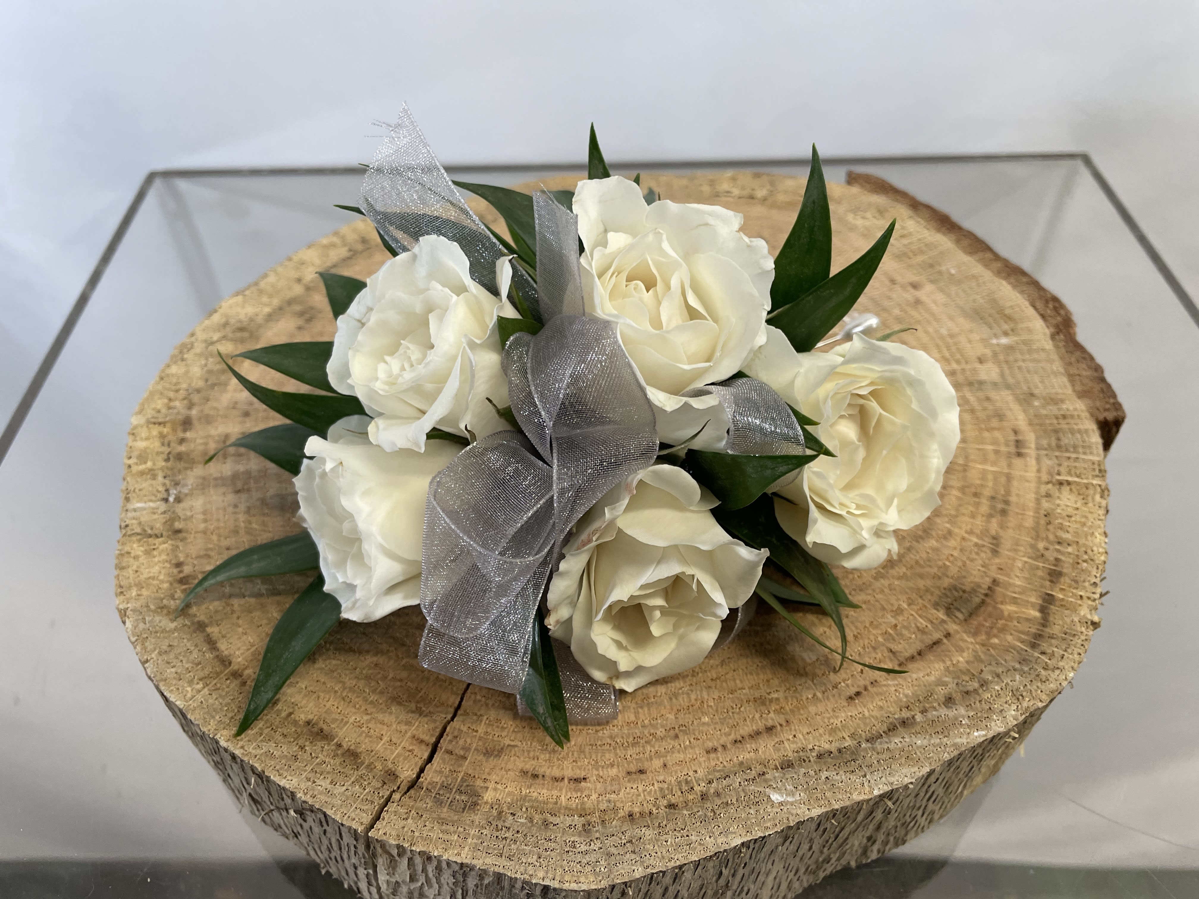 White rose bouquet with silver ribbon on a wood slice