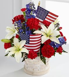Red, white, and blue floral arrangement in a white basket with American flags