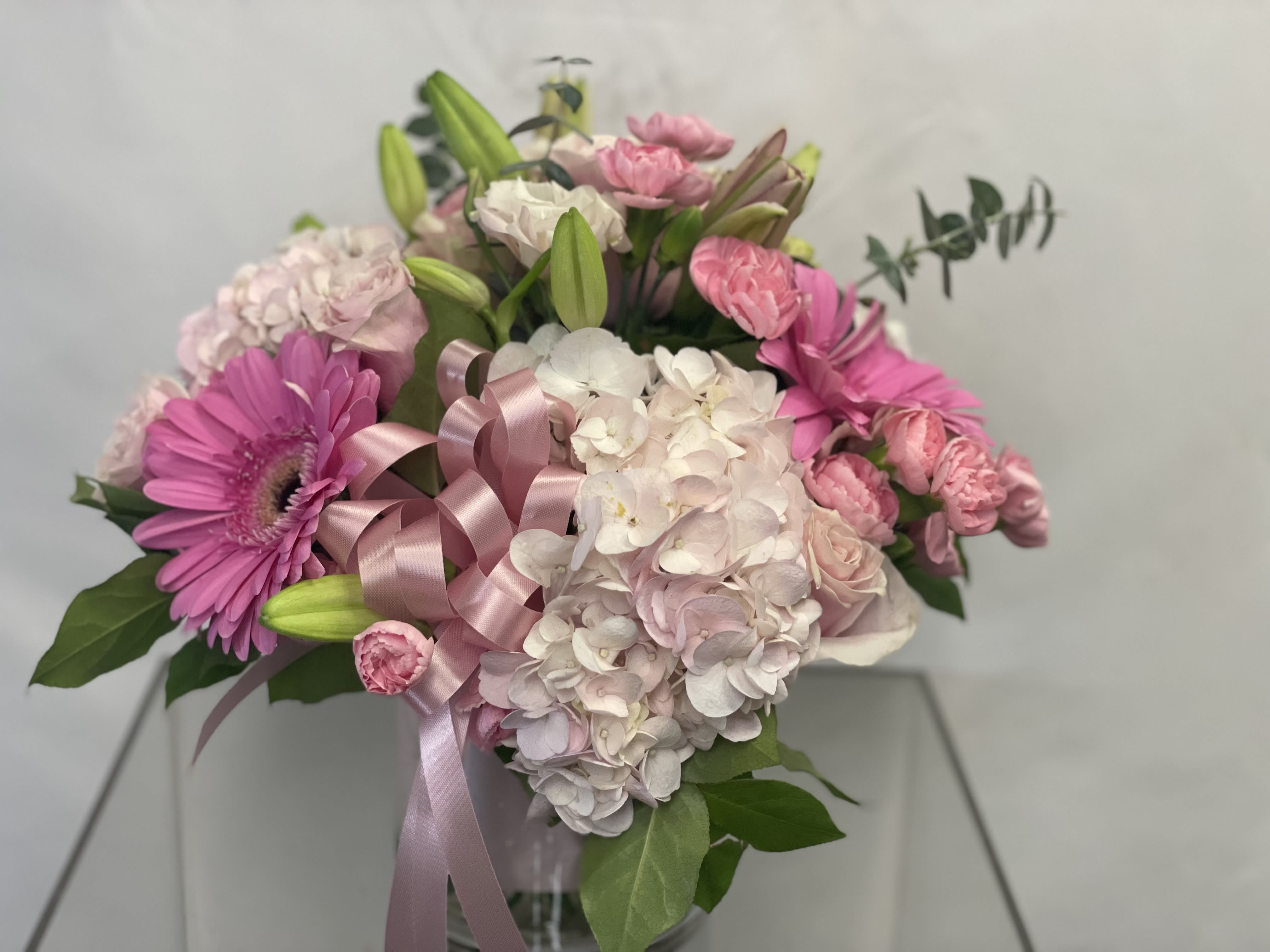 Pink and white bouquet with lilies, hydrangeas, and a ribbon in a vase