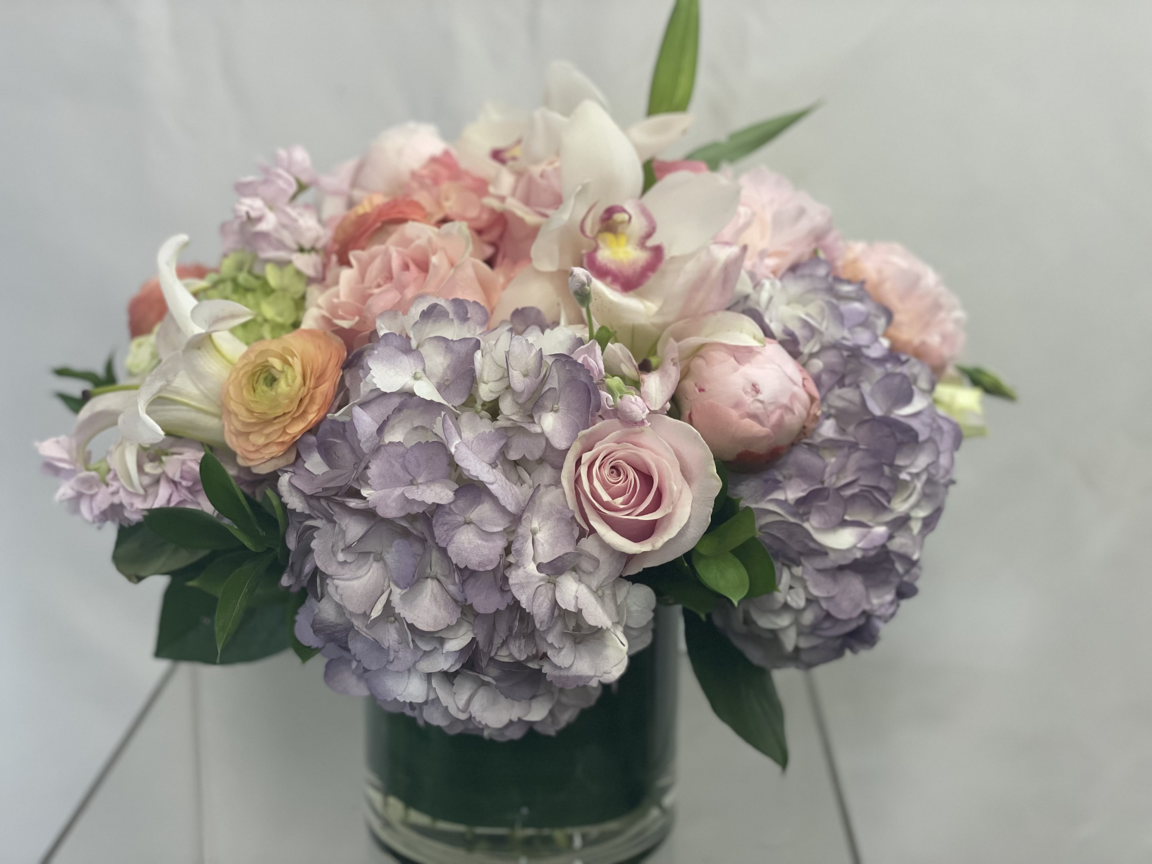 Pastel bouquet of hydrangeas, roses, and orchids in a glass vase
