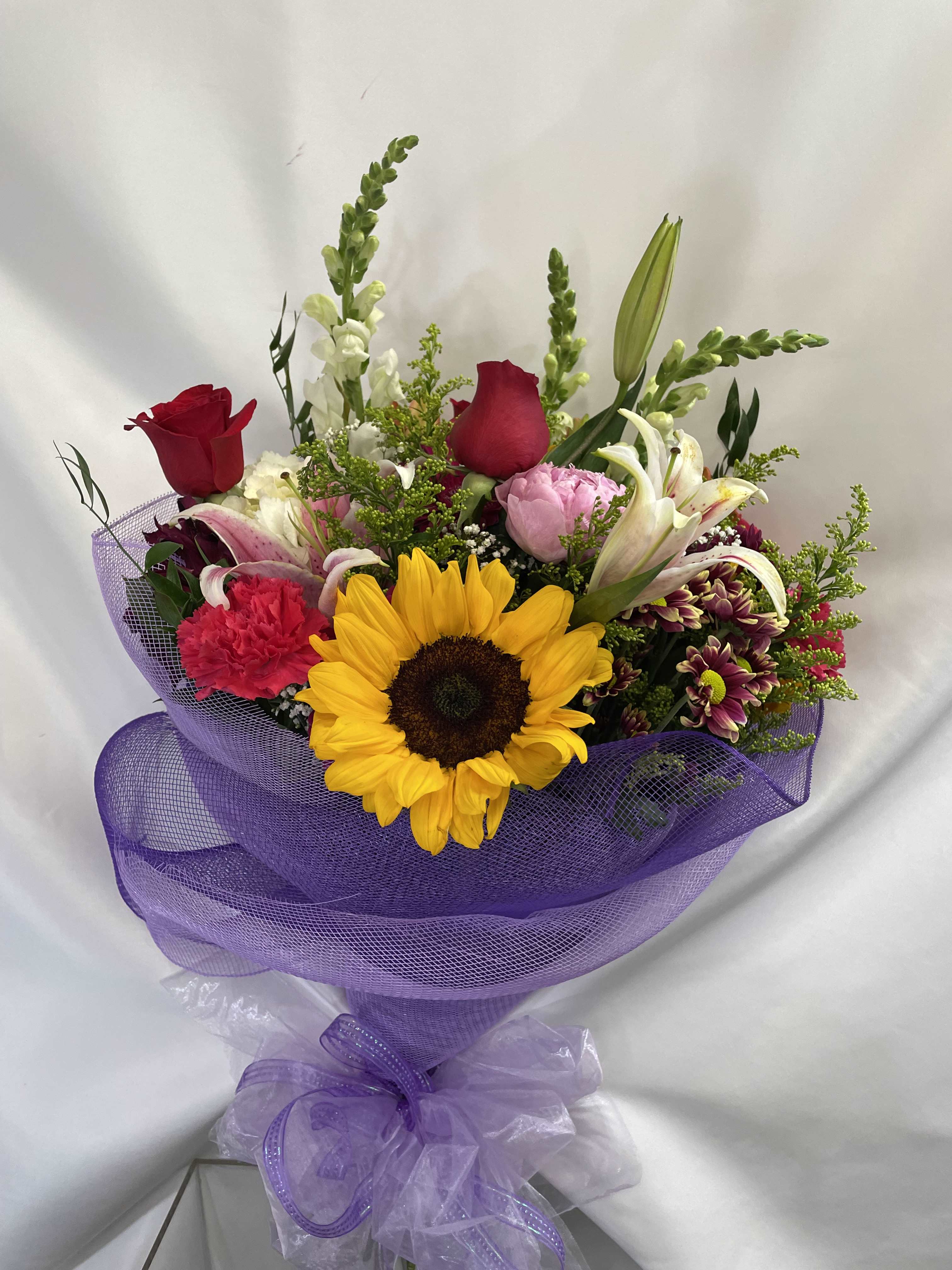 Mixed bouquet with a sunflower, roses, lilies, and purple wrapping