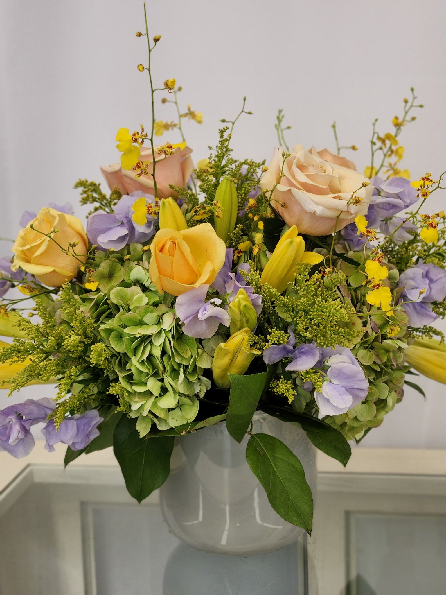Pastel bouquet of roses, hydrangeas, and yellow orchids in a white vase