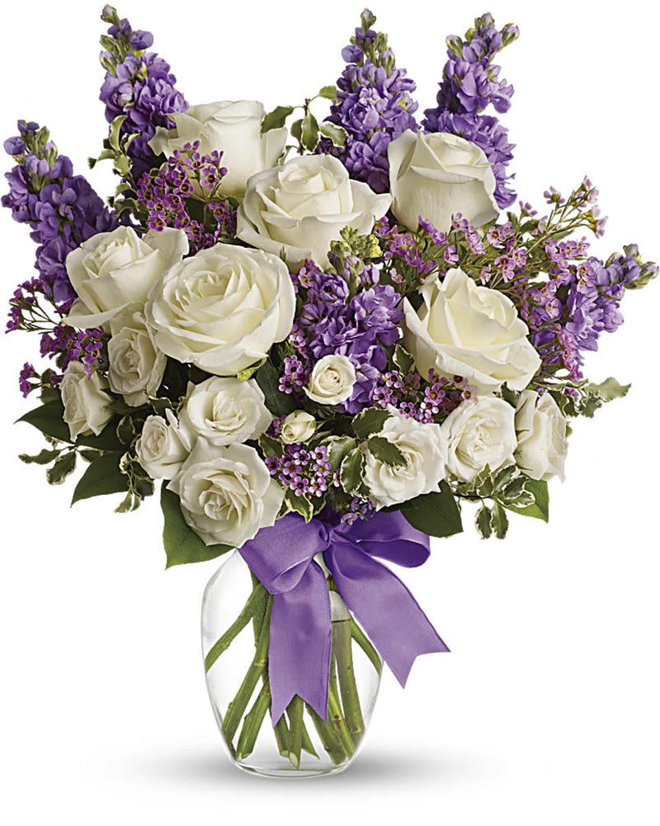 White roses and purple flowers in a glass vase with a purple ribbon