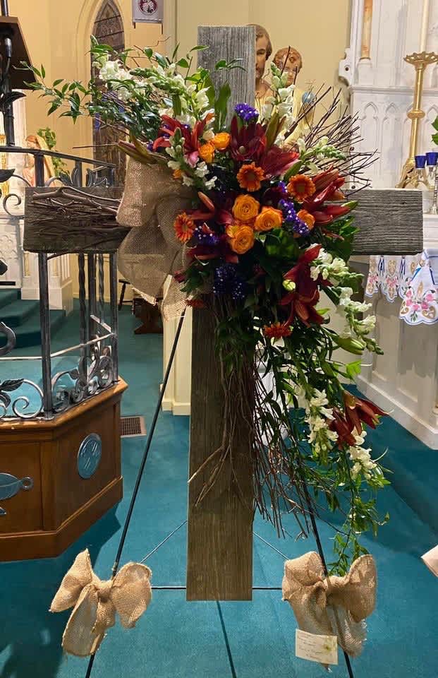 Large floral cross arrangement with orange, red, white, and purple flowers