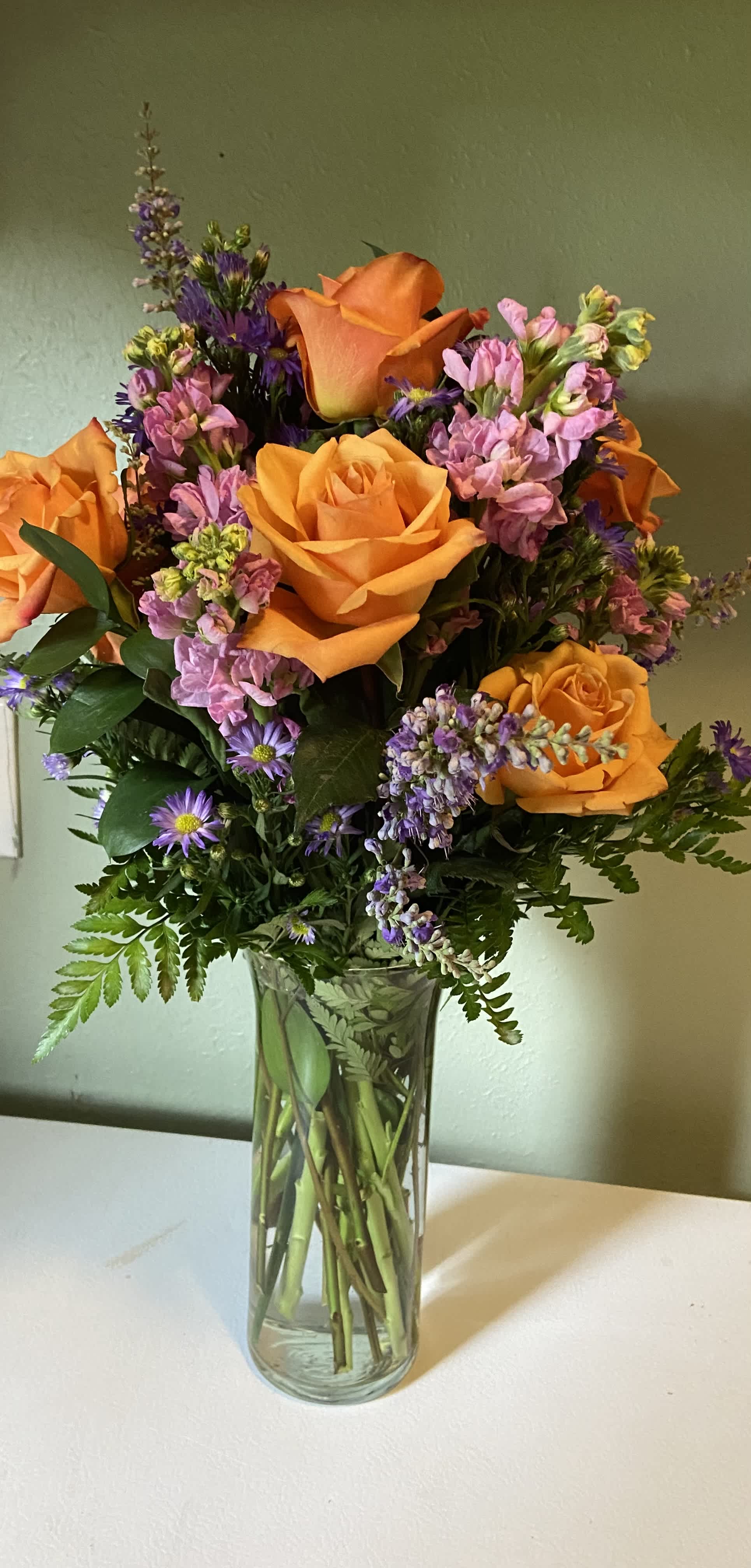 Orange roses and purple flowers in a clear glass vase
