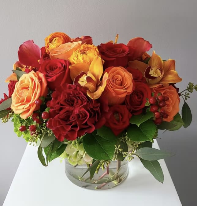 Bouquet of red and orange roses with orchids in a glass vase