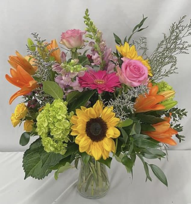 Mixed bouquet with sunflowers, pink roses, orange lilies, and a glass vase