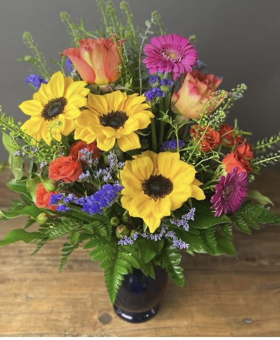 Colorful bouquet of sunflowers, roses, and gerbera daisies in a dark vase