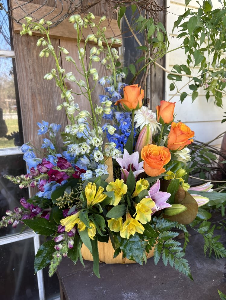 Mixed bouquet with orange roses, lilies, and blue flowers in a basket