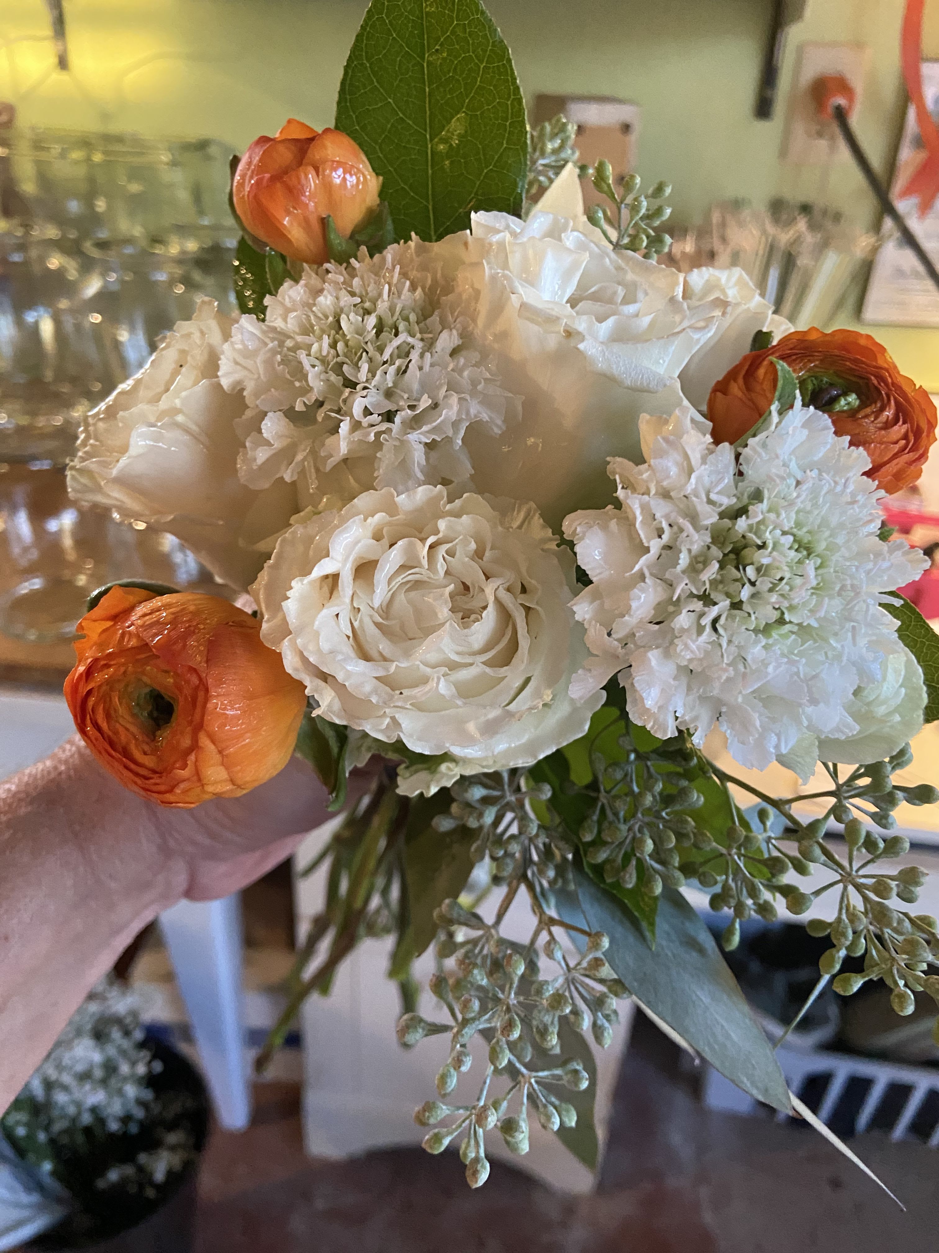 Handheld bouquet of white roses, white blooms, and orange ranunculus