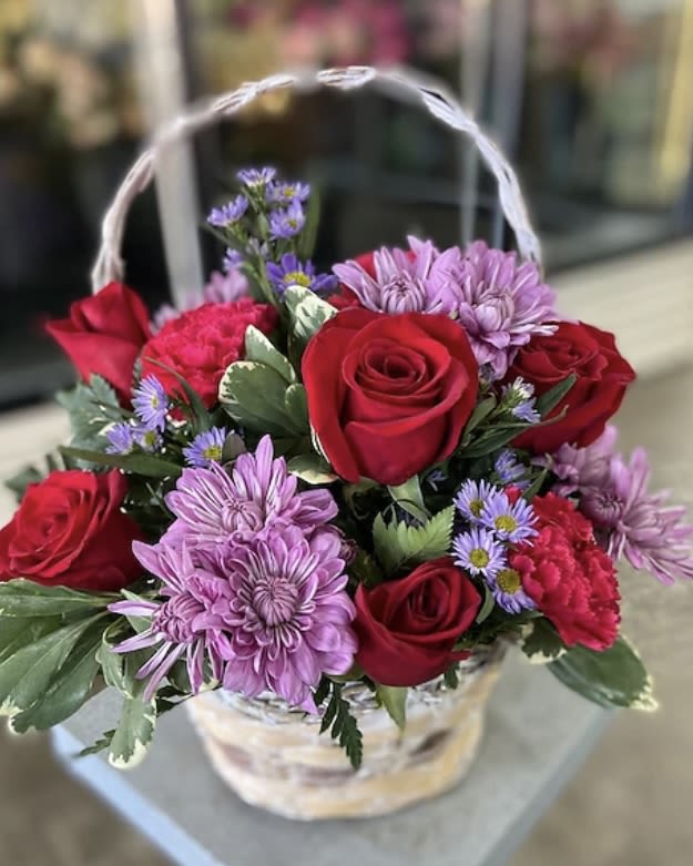 Basket of red roses and purple daisies with a white handle