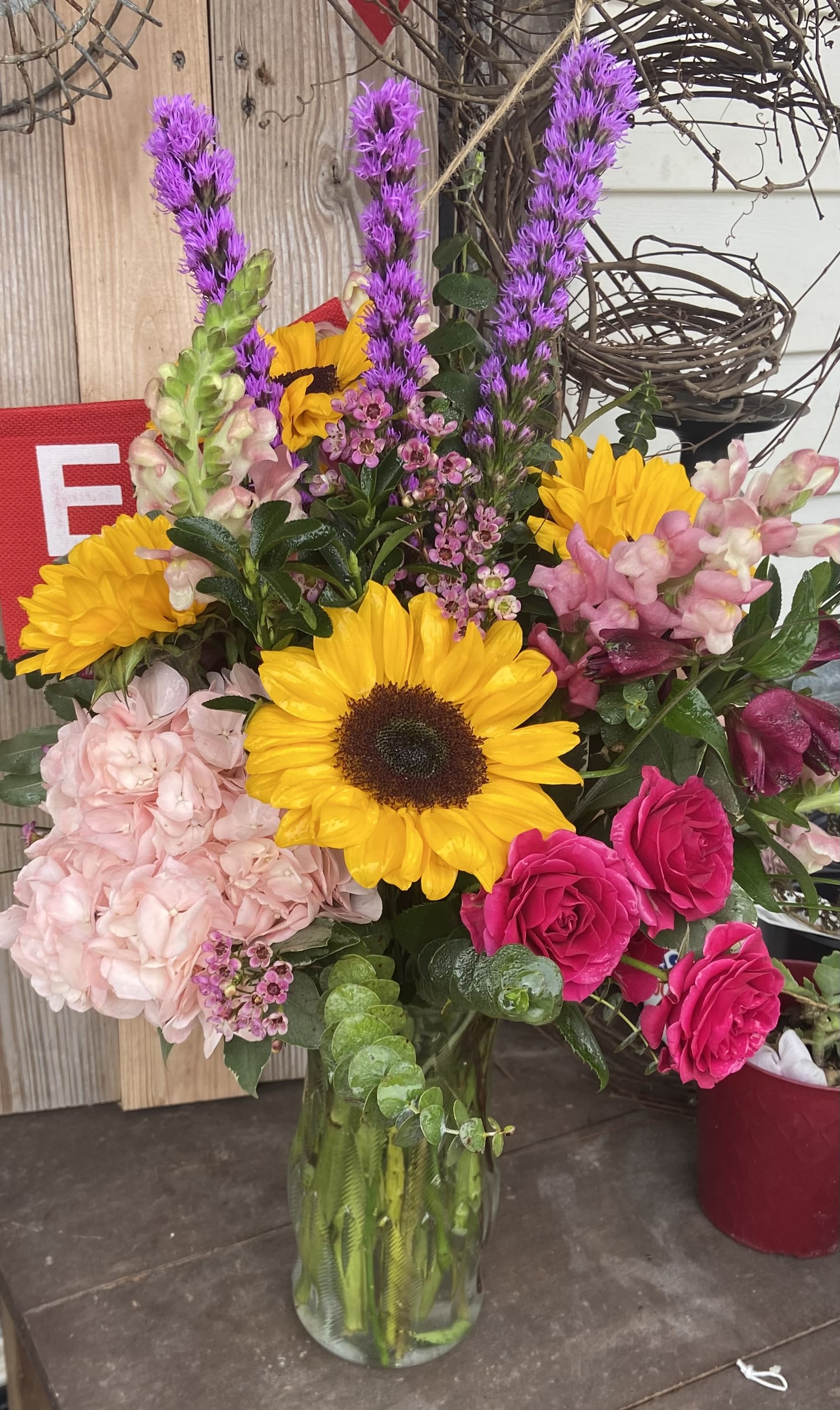Mixed bouquet with sunflowers, pink roses, hydrangea, and purple spikes in a glass vase