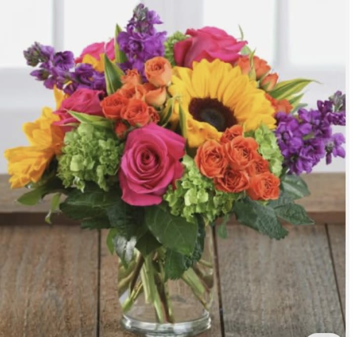 Colorful bouquet of roses, sunflowers, and purple flowers in a glass vase