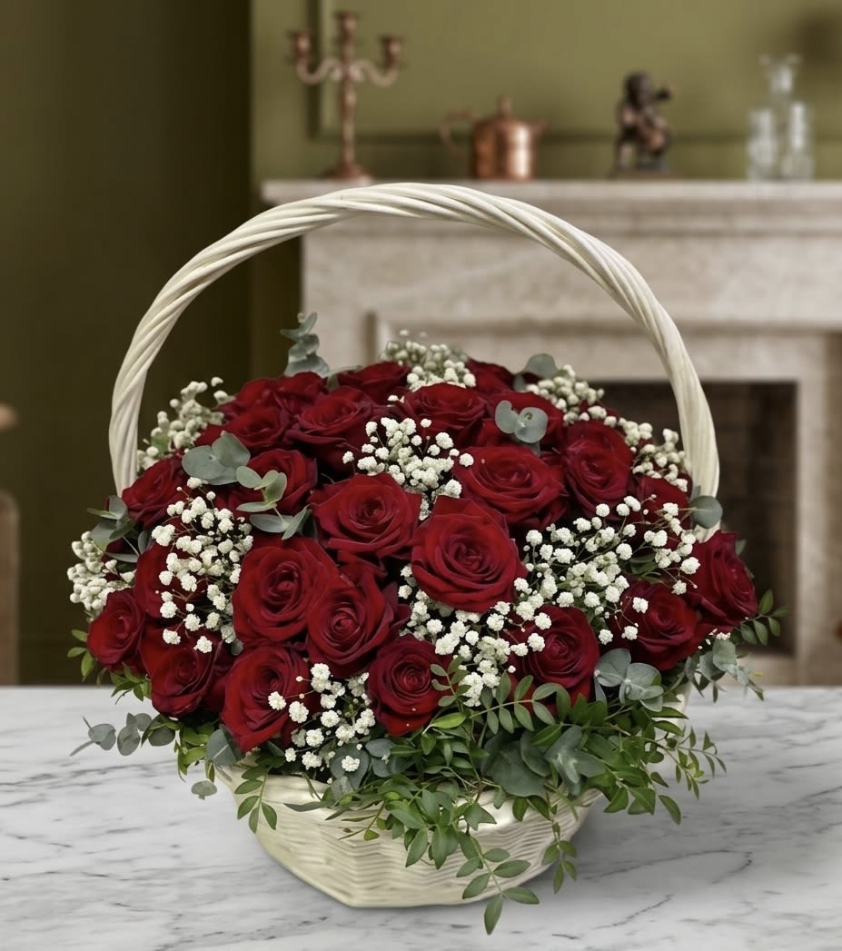 Midnight Rose Basket  - Bring a touch of classic elegance to your space with this stunning arrangement of deep red roses and delicate baby’s breath. Nestled in a handcrafted white wicker basket, this timeless piece is designed to serve as a sophisticated centerpiece for any occasion, from intimate home gatherings to professional corporate events. The rich, velvety texture of the roses is beautifully complemented by lush greenery and the ethereal charm of white fillers, creating a balanced and luxurious aesthetic. • Premium Selection: Features high-quality red roses at the peak of their bloom. • Artisanal Design: Expertly arranged to showcase a full, rounded silhouette. • Versatile Decor: Perfect for mantels, dining tables, or as a thoughtful gift for someone special.