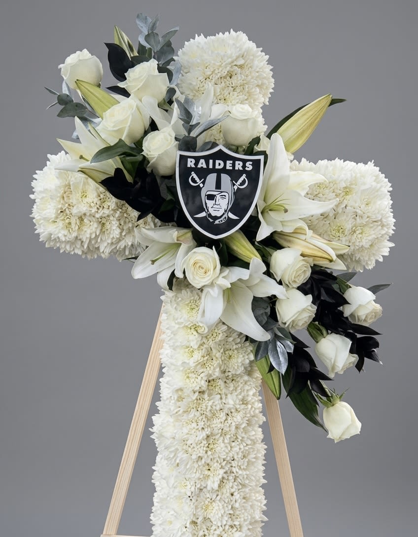 Raider Tribute Cross  - Honor a lifelong fan with a striking, heartfelt tribute. This elegant standing floral cross is beautifully handcrafted with premium white mums, roses, and lilies, accented by deep greenery and a Raiders shield emblem. A powerful and memorable statement of devotion, expertly designed to bring comfort and honor their legacy.