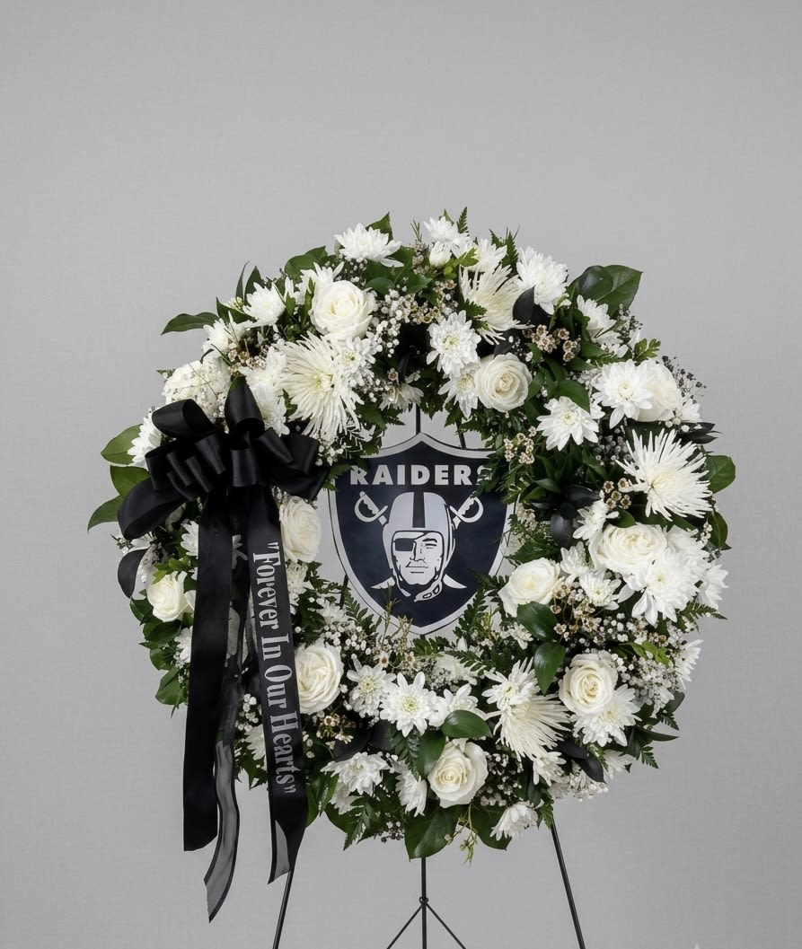 Raider Tribute Wreath  - A beautiful, custom funeral wreath honoring a devoted fan. This elegant circular arrangement features a serene blend of fresh white roses, spider mums, and delicate baby's breath. Accented with lush greens and a sophisticated black ribbon—available with a personalized script like "Forever in Our Hearts"—this heartfelt tribute centers around a prominent Raiders logo, offering a dignified, powerful way to celebrate their legacy and team spirit.