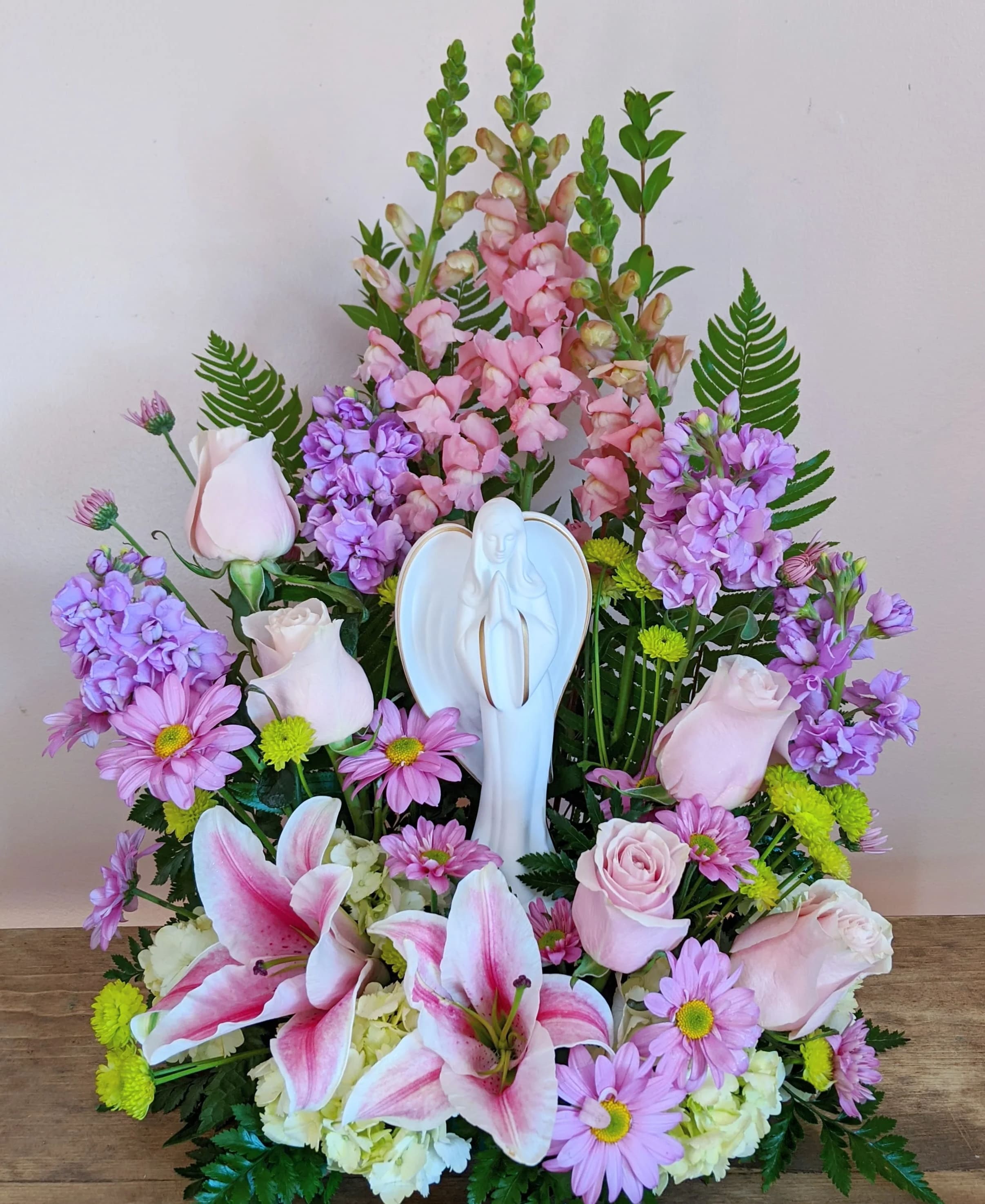 Pink and purple floral arrangement with lilies and roses around a white angel figurine