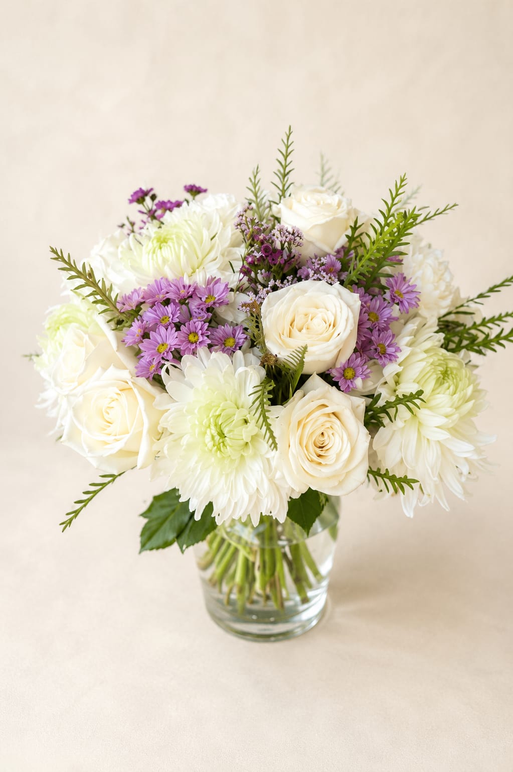 Themis' Serenity – Luxury White Vase Arrangement - Inspired by Themis, the Greek goddess of harmony and balance, this arrangement reflects quiet elegance through its timeless palette of white blooms and delicate lavender accents.  Designed in Flower Fairy's signature garden style, this luxury vase arrangement features premium white roses, elegant white chrysanthemums, lavender asters, seasonal flowers, and fresh greenery. The soft contrast of crisp white and gentle lavender creates a naturally balanced composition with graceful texture and understated sophistication. Arranged in a clear glass vase, this design complements any home, office, or special celebration.  Perfect for birthdays, thank-you gifts, sympathy, get well wishes, housewarmings, anniversaries, or simply sending a thoughtful expression of care.  Each arrangement is handcrafted by Flower Fairy using the freshest flowers available. While occasional substitutions may be necessary due to seasonal availability, we always preserve the overall style, color palette, and premium quality of every design.  Features: Luxury vase arrangement Premium white roses White chrysanthemums Lavender asters Seasonal flowers Garden-style floral design Glass vase Handcrafted by Flower Fairy Same-day flower delivery in Phoenix