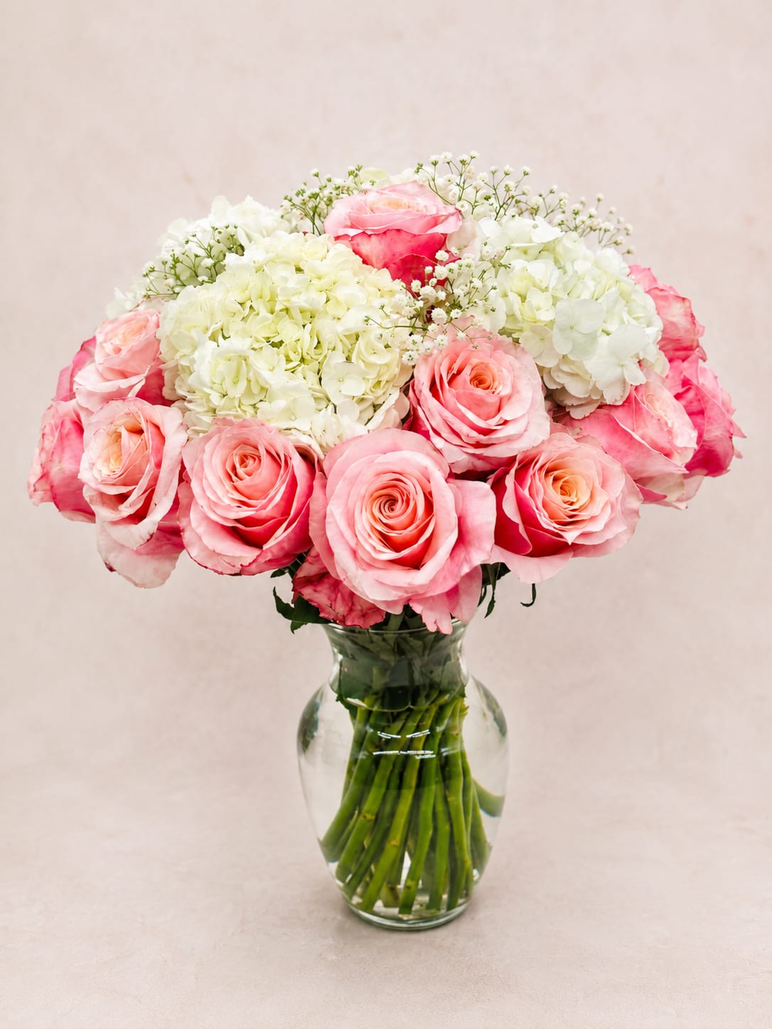 Lada's Enchanting Charm – Luxury Vase - Inspired by Lada, the Slavic goddess of love, beauty, and spring, this graceful arrangement captures the gentle romance of blooming gardens and heartfelt affection.  Lada's Enchanting Charm showcases luxurious premium pink roses nestled among lush white hydrangeas and delicate baby's breath, creating a timeless design filled with softness and elegance. Carefully handcrafted in a classic glass vase, this arrangement radiates warmth, beauty, and refined simplicity.  Perfect for birthdays, anniversaries, Mother's Day, welcoming a new baby, congratulations, or simply expressing love and appreciation. Its romantic color palette makes it a memorable gift for life's most meaningful moments.  Every arrangement is handcrafted by Flower Fairy using the freshest premium flowers available. Seasonal substitutions may occasionally be necessary while preserving the overall style, color palette, and value of the design.  Features: Premium pink roses Lush white hydrangeas Delicate baby's breath accents Elegant glass vase Handcrafted by Flower Fairy Available in Standard, Deluxe, and Premium sizes Same-day flower delivery throughout the Phoenix Metro Area
