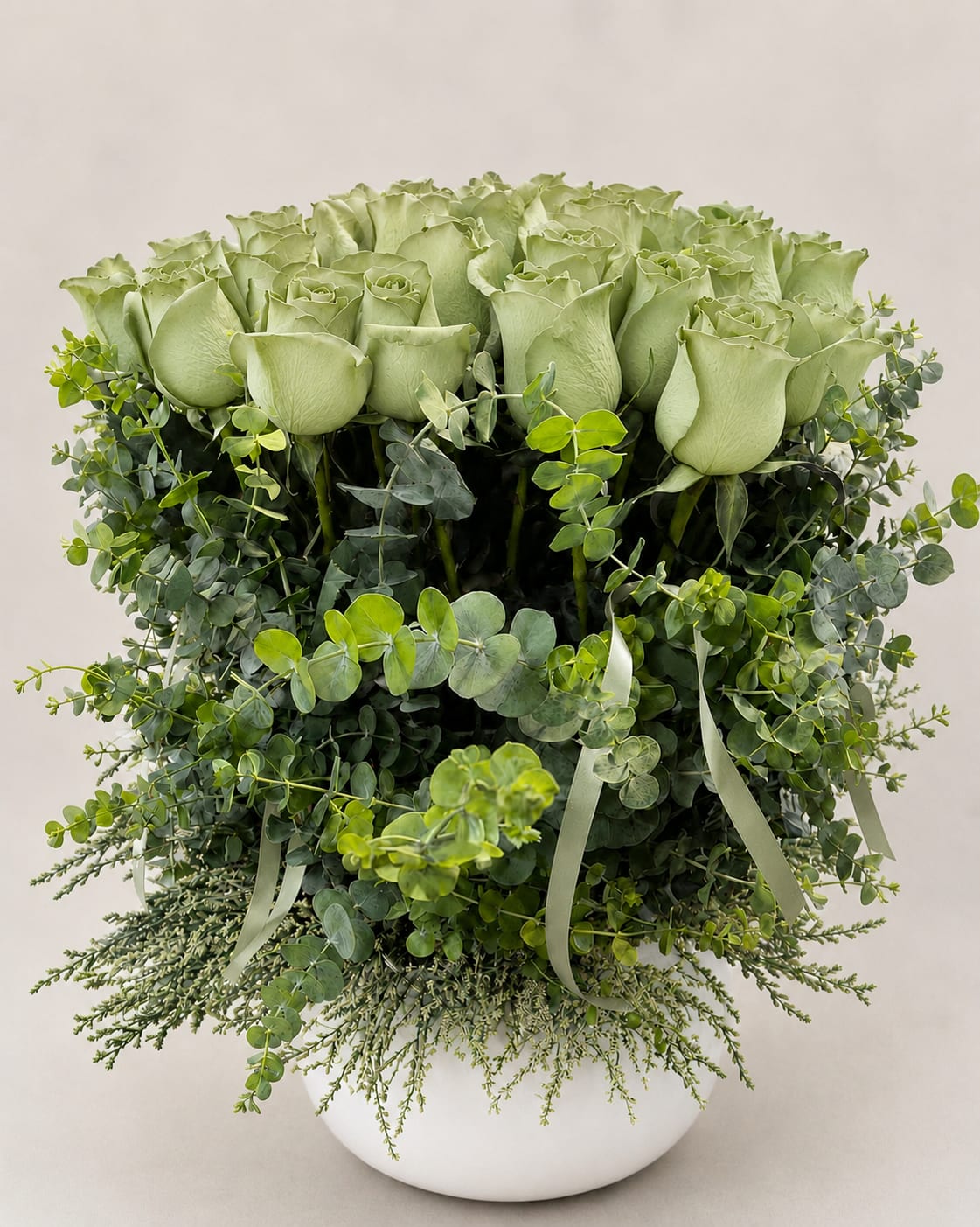 Arrangement of pale green roses in a white vase with trailing greenery
