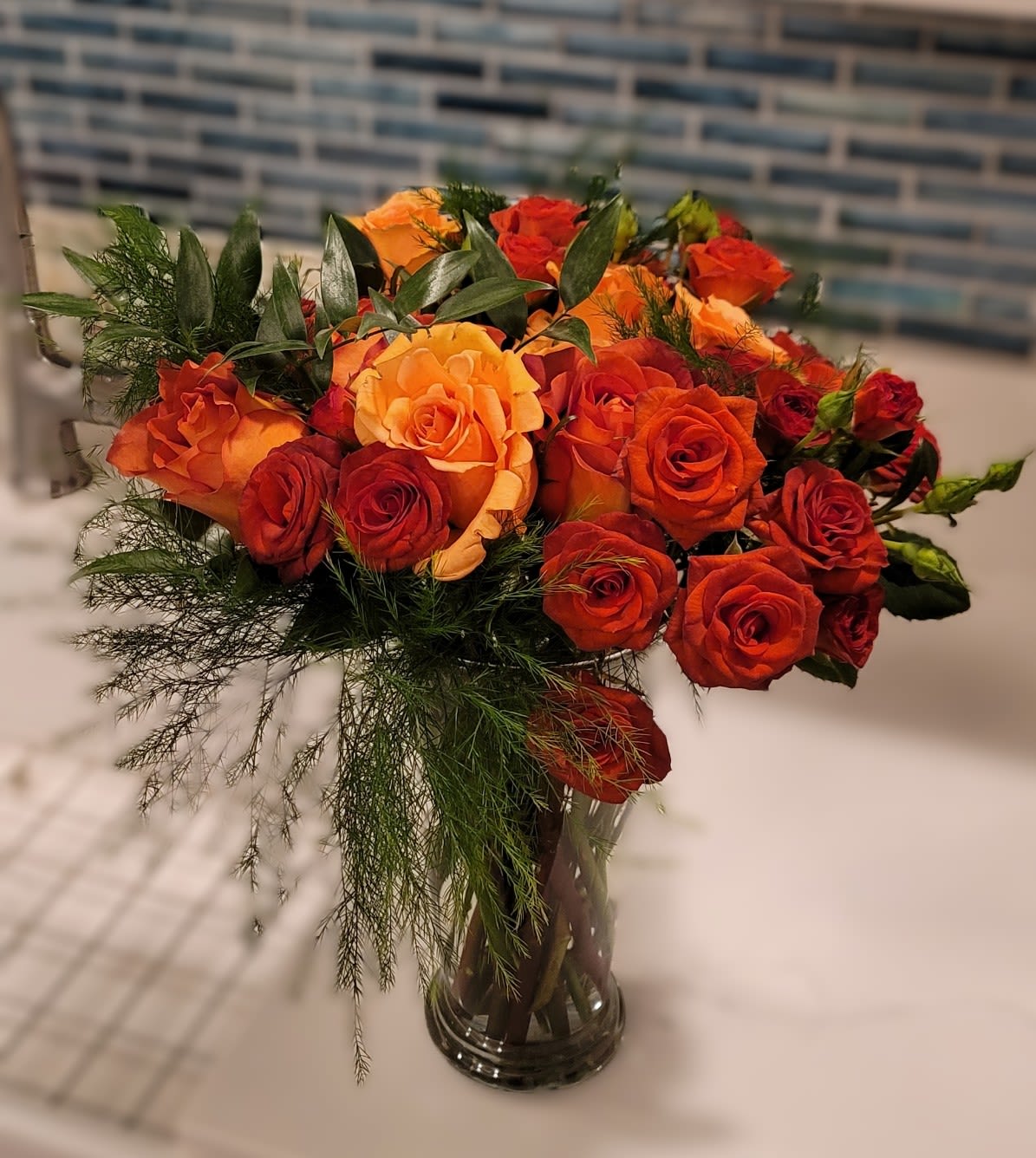 Orange and red roses arranged in a clear glass vase