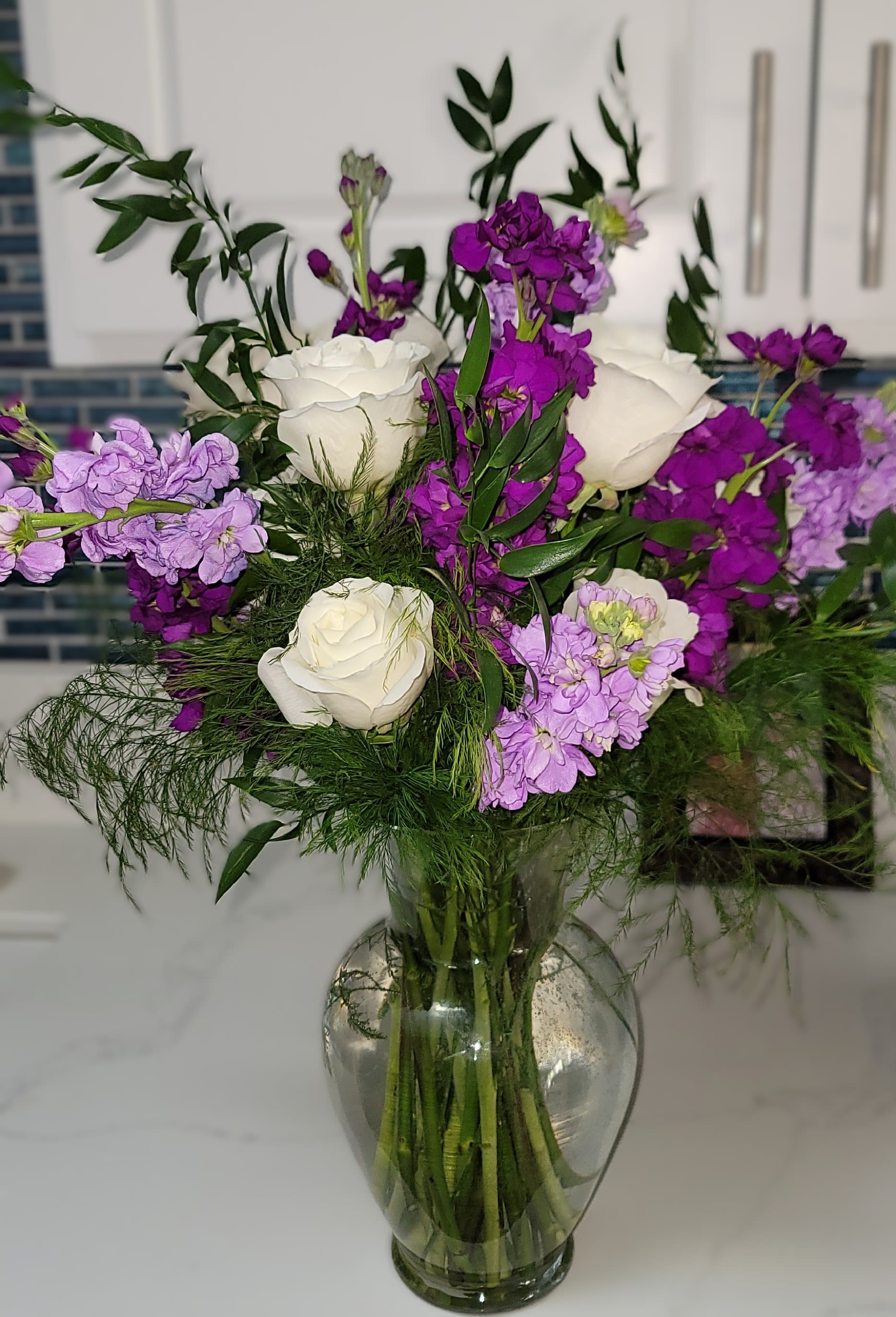White roses and purple flowers arranged in a clear glass vase