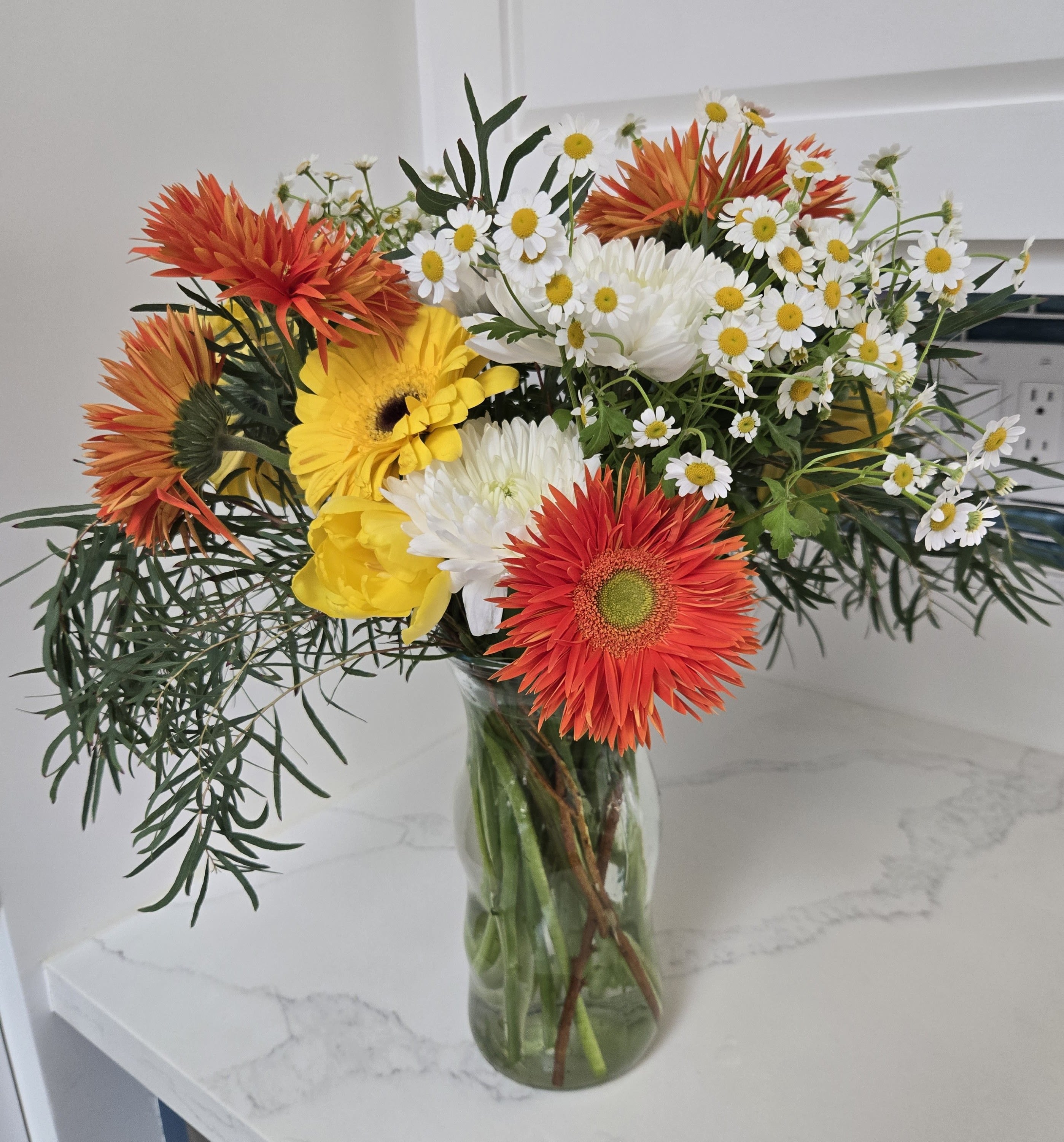 Bouquet of orange, yellow, and white flowers in a glass vase