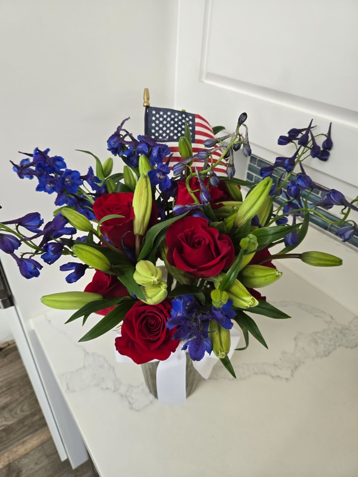 Red roses and blue flowers in a clear vase with an American flag