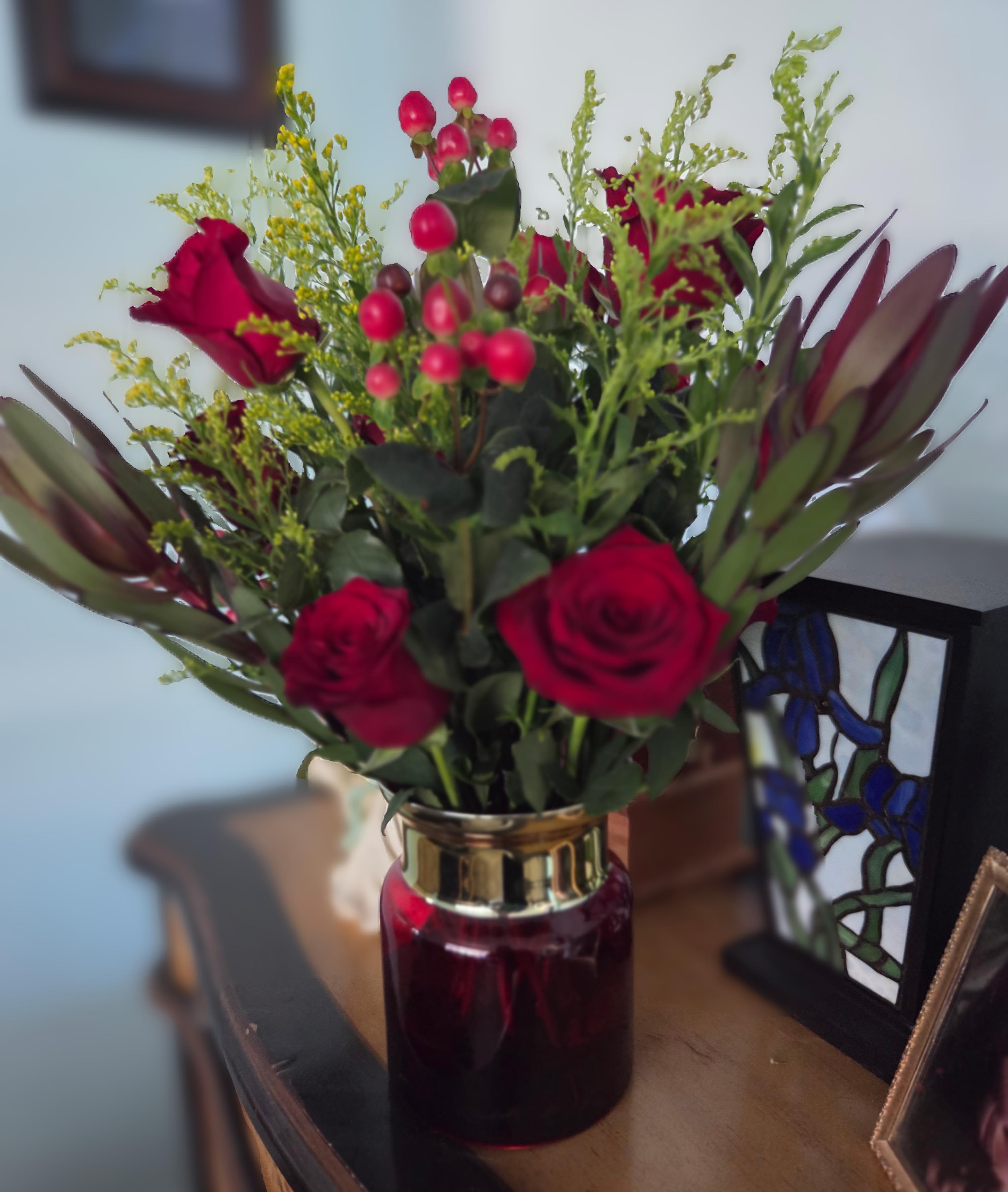 Red roses and berry stems arranged in a glass vase