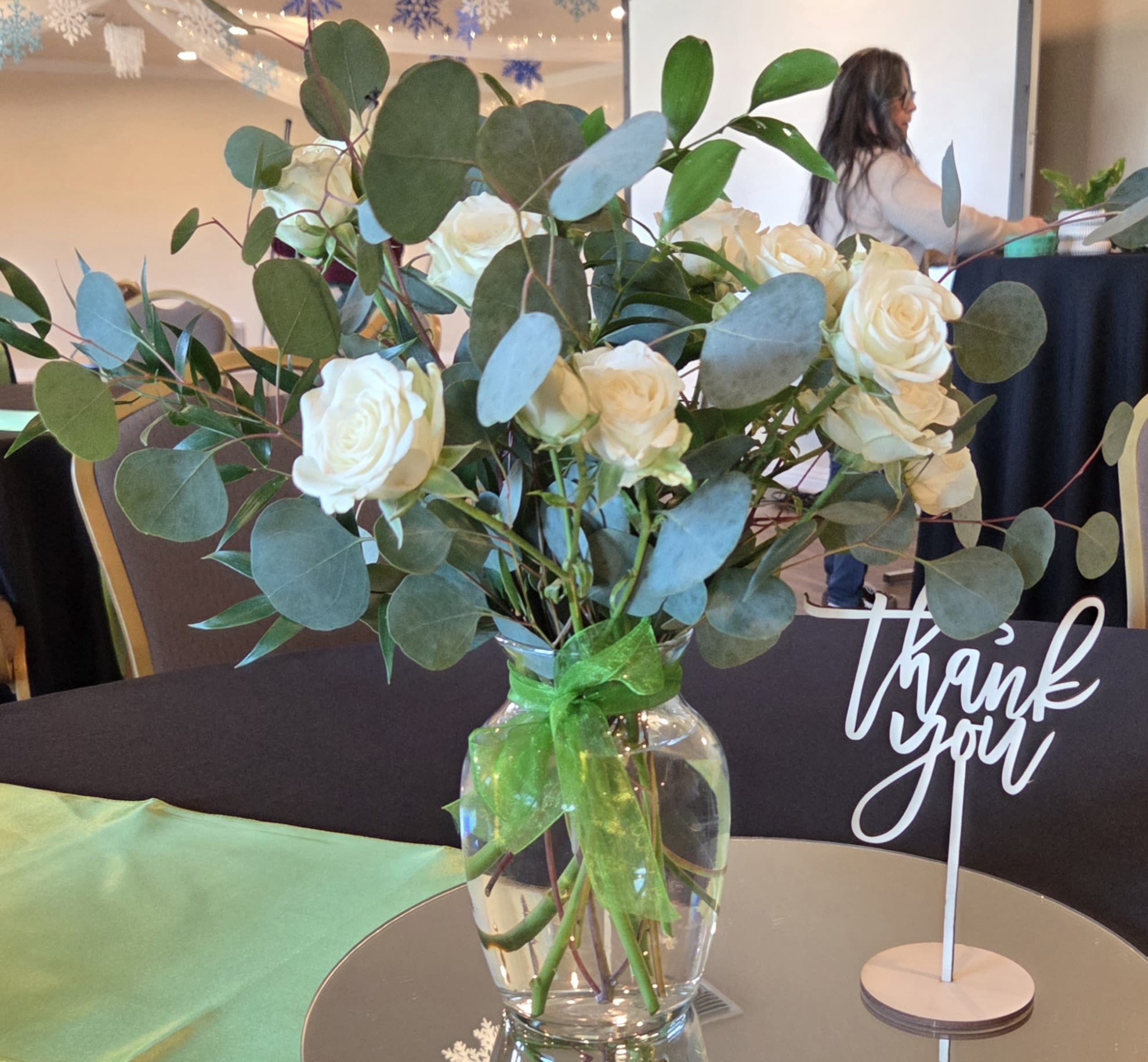 White roses in a clear glass vase with eucalyptus and a green ribbon