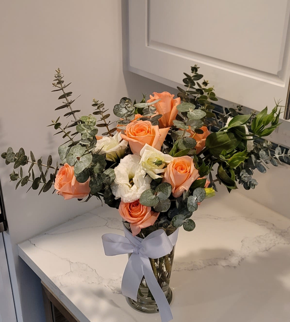 Peach and white roses arranged in a clear glass vase with a ribbon.