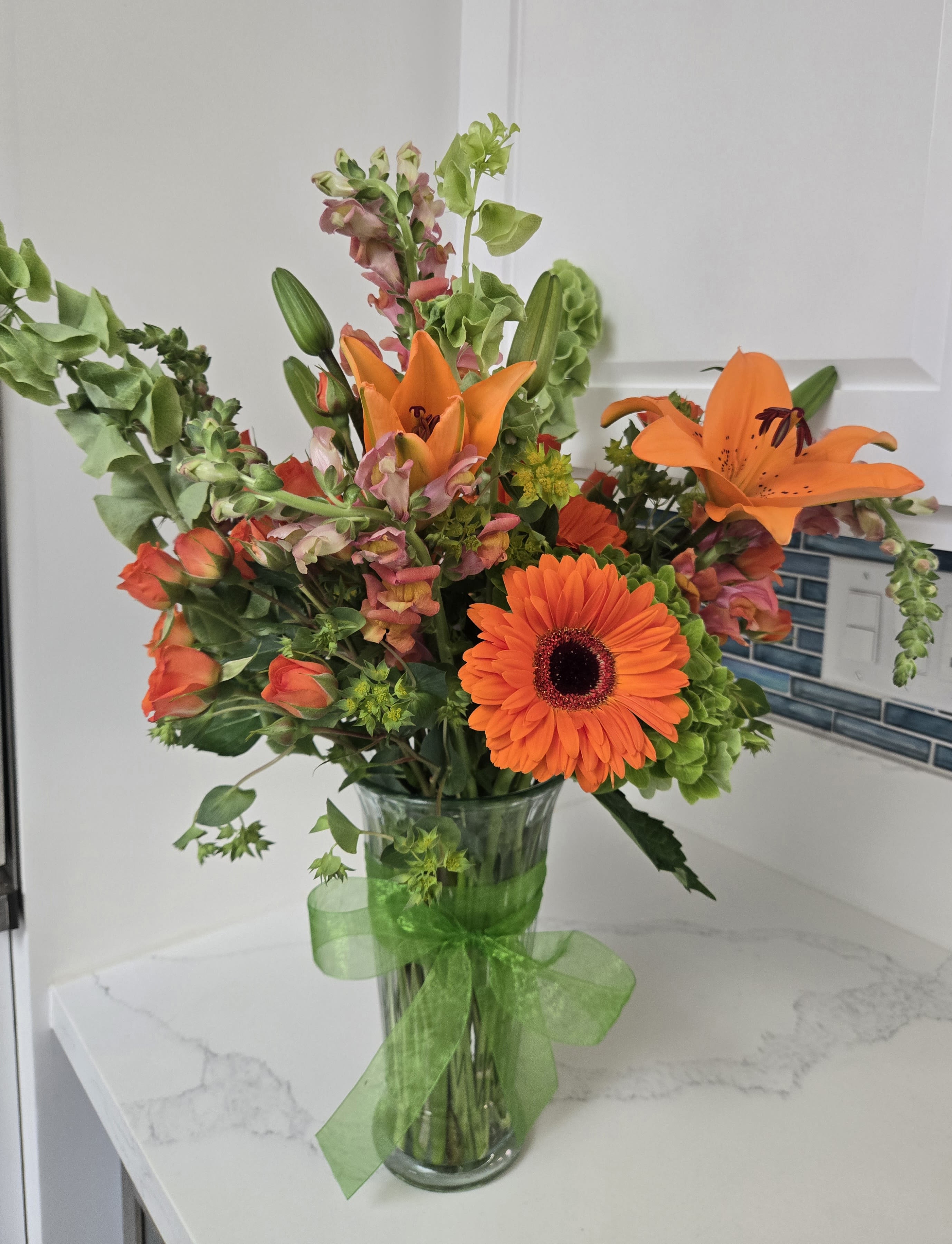 Orange mixed bouquet in a clear glass vase with a green ribbon