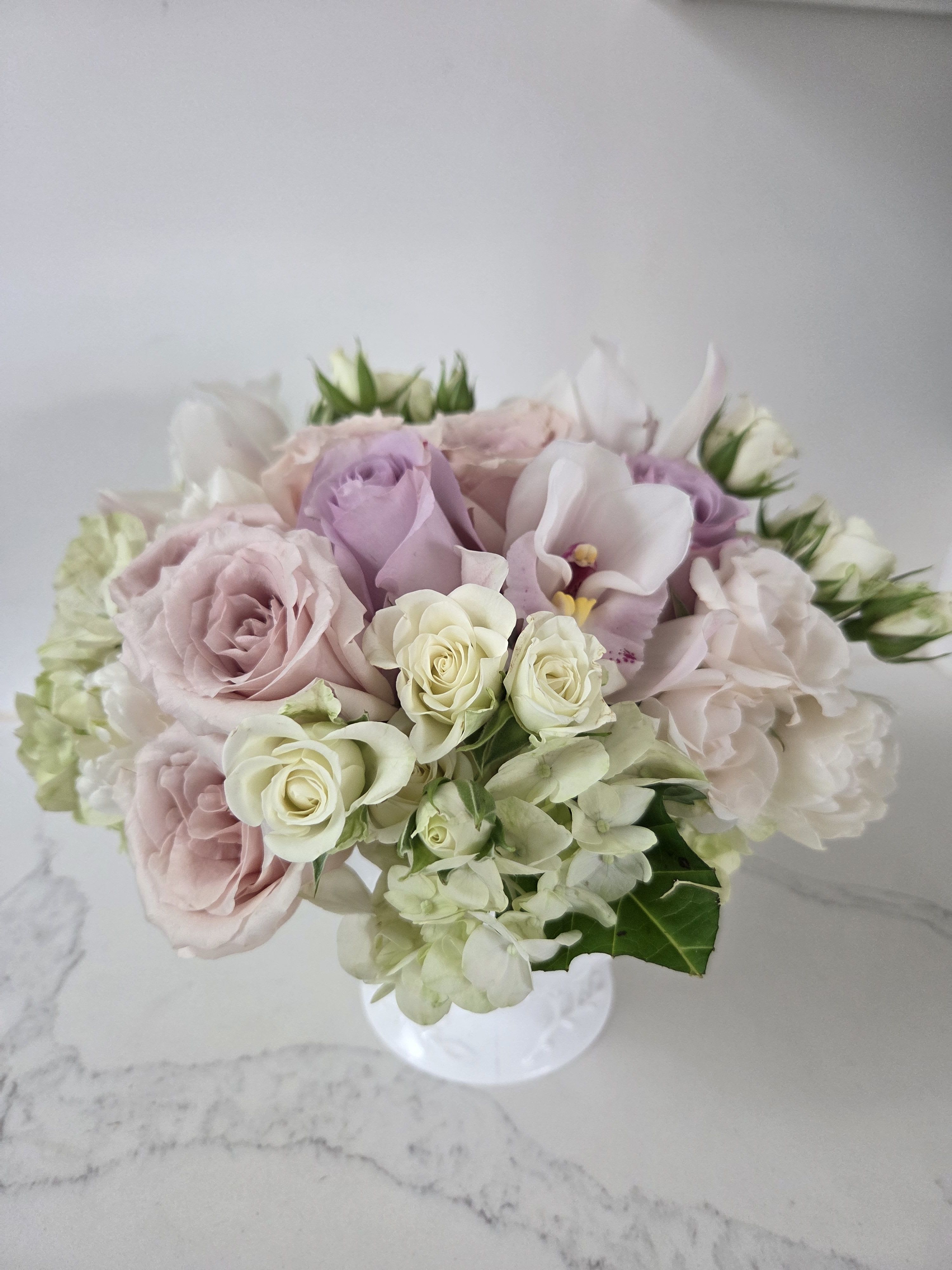 Sweet Caroline - Filled with over 18 stems of exquisite soft pastel roses, white tulips, spray roses, hydrangea and orchids that come together to create a delicate gift.  Displayed in a white vase.      