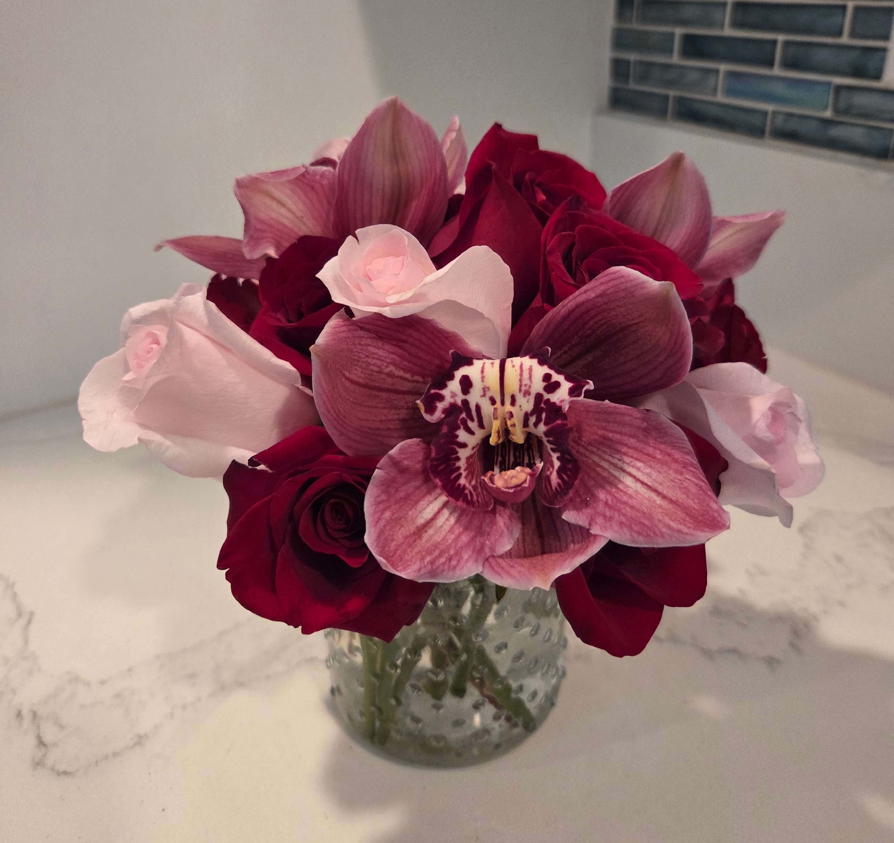 Bouquet of red roses and pink orchids in a glass vase