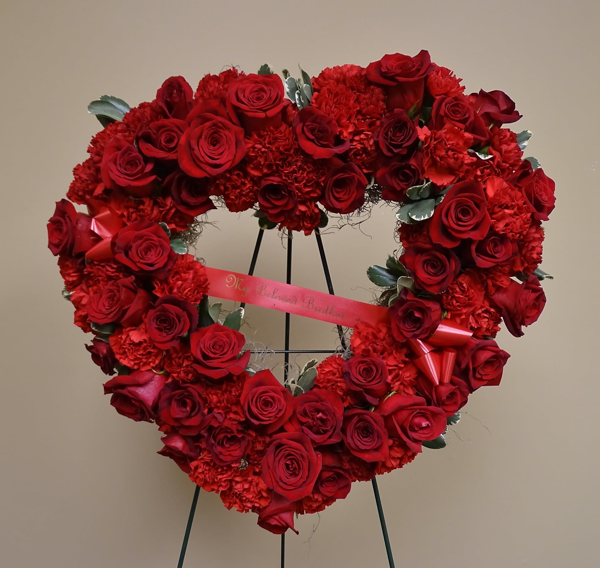 Heart-shaped red rose wreath on a stand with a ribbon