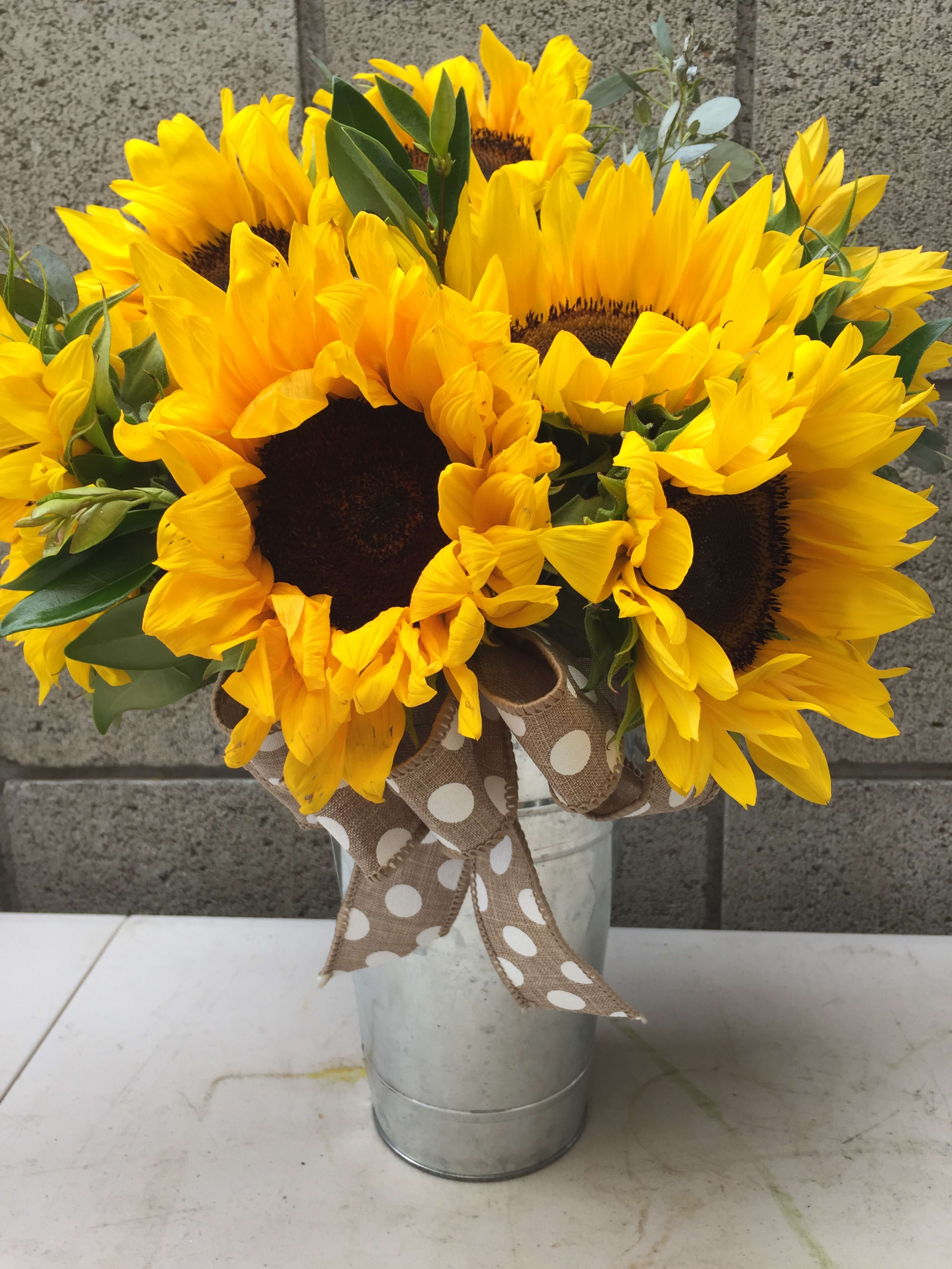 Bouquet of bright yellow sunflowers in a metal bucket with a polka-dot ribbon