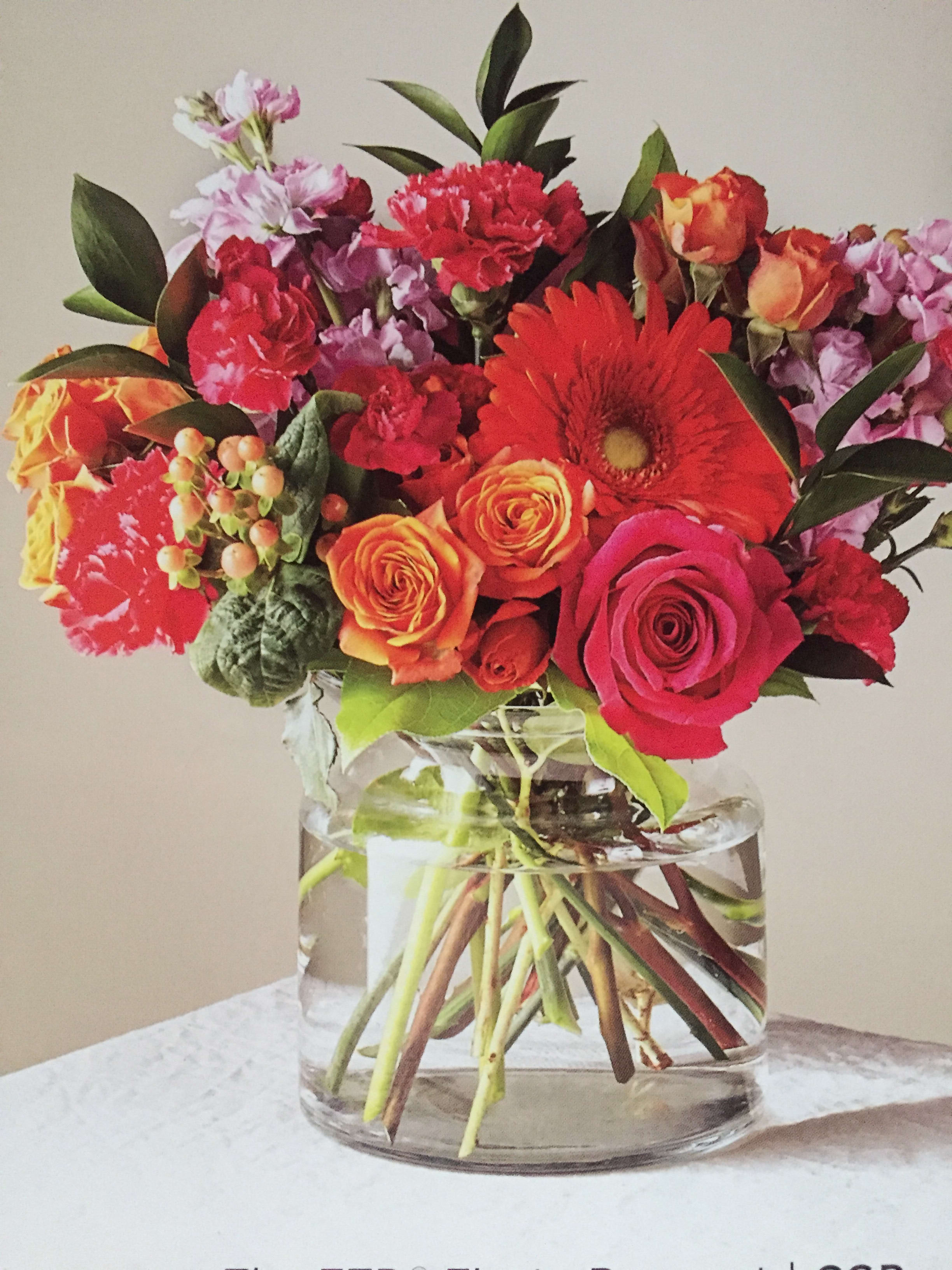 Mixed bouquet of red, orange, and pink flowers in a clear glass vase