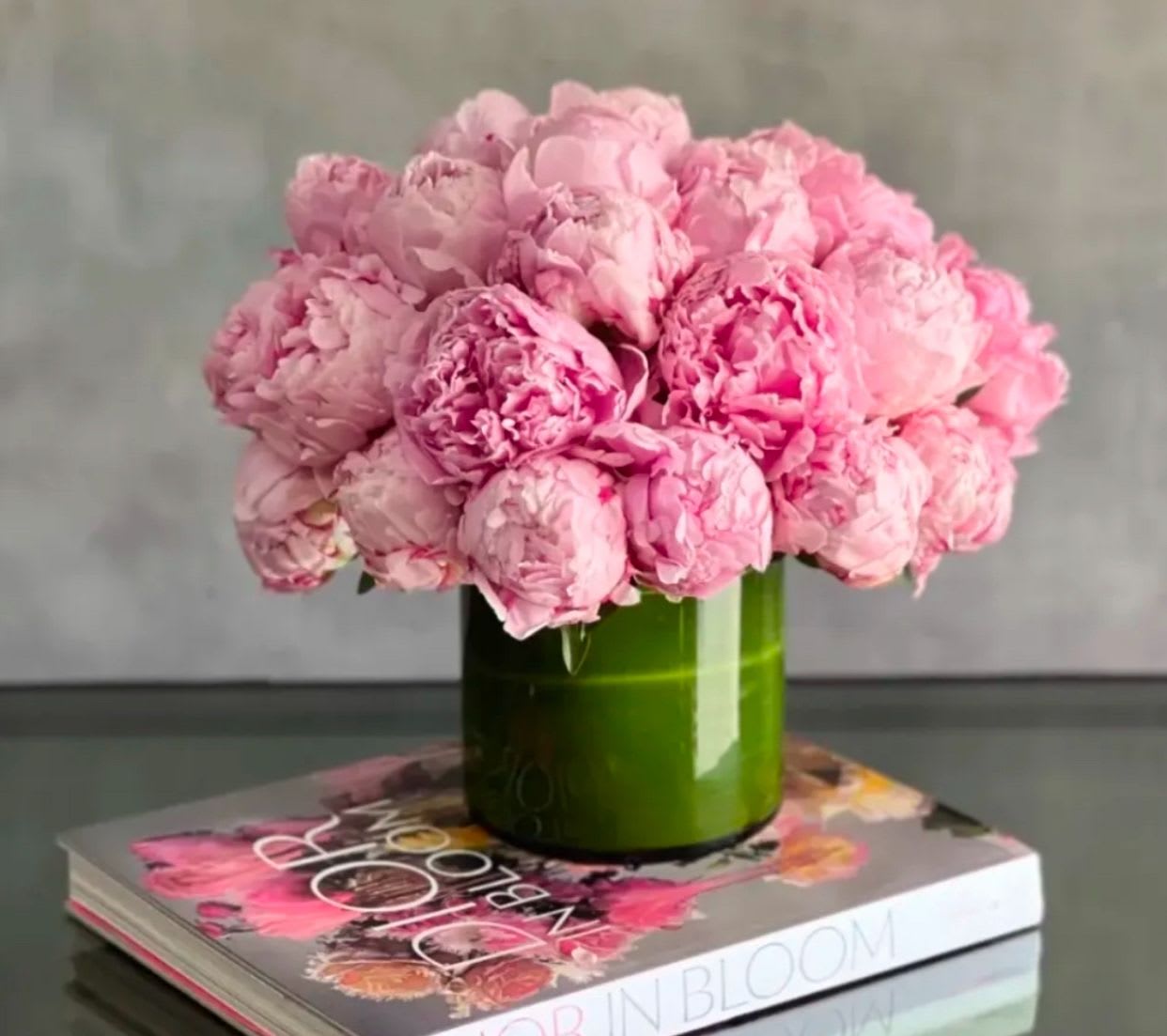 Tight cluster of pink peonies in a green cylinder vase set on a floral coffee table book