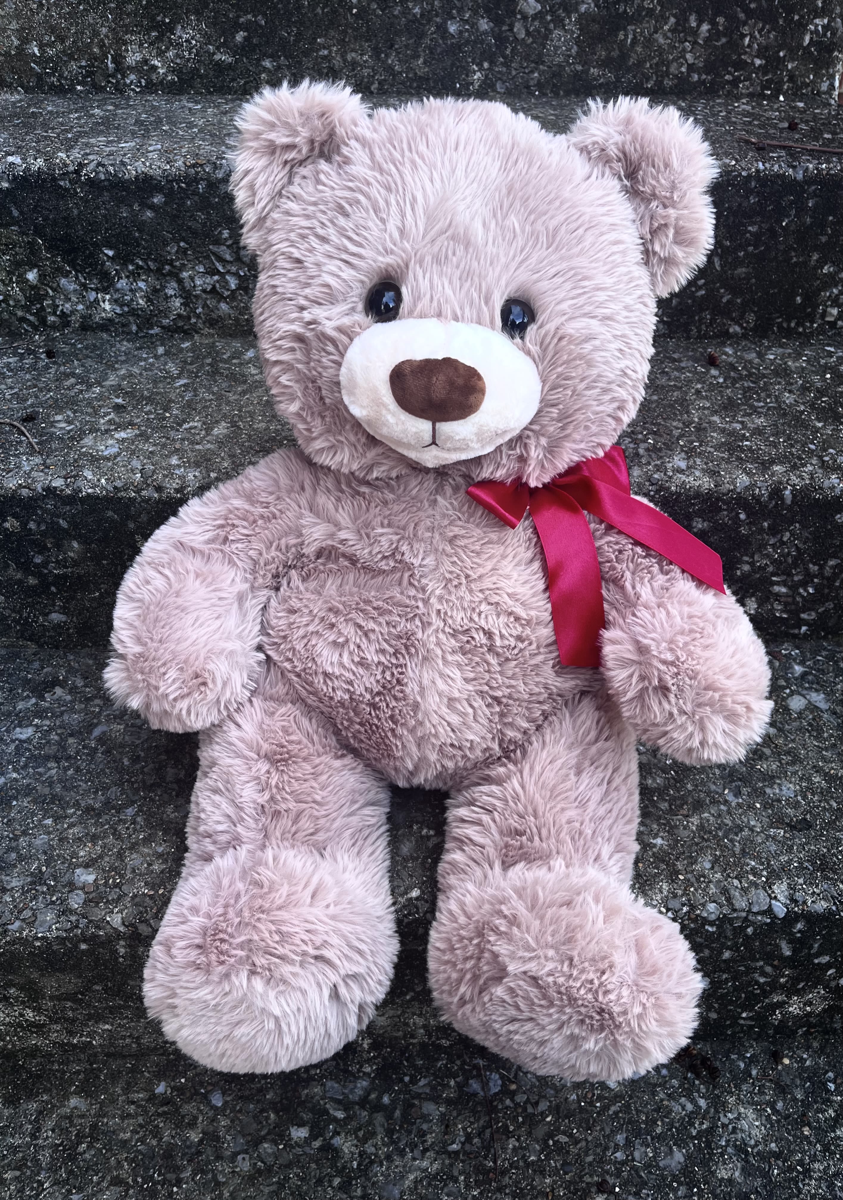 Pink teddy bear with a red ribbon sitting on stone steps