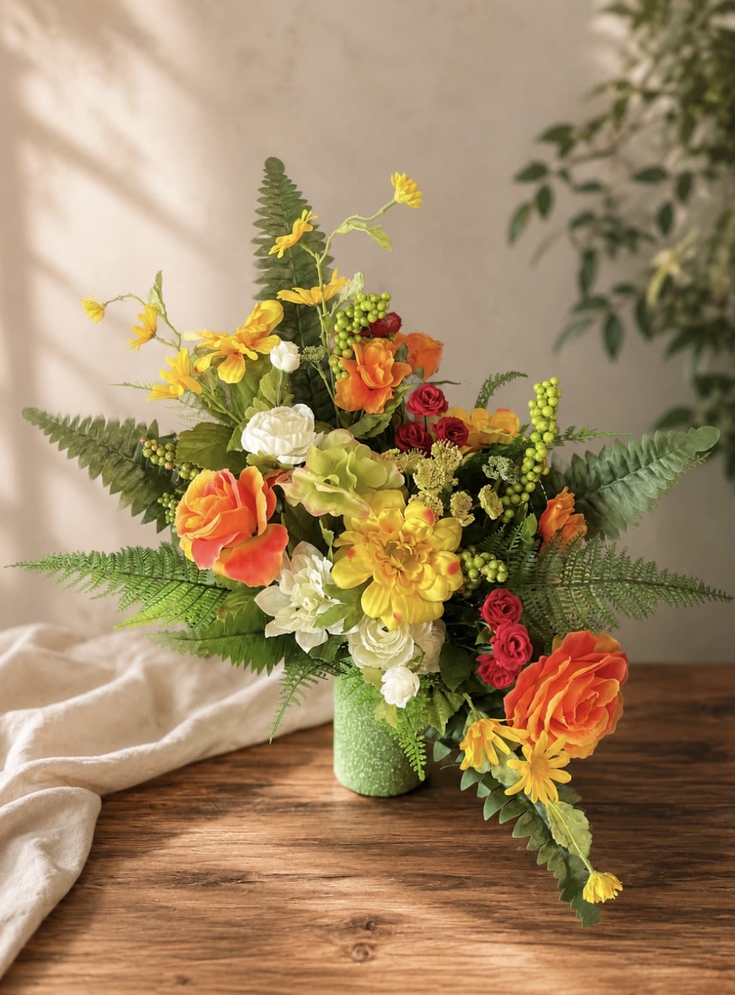 (Silk) Sunshine  - Vibrant orange roses and sunny yellow daisies create an immediate burst of warmth in this silk flower arrangement, ideal as a birthday bouquet, congratulations gift, or cheerful thank-you surprise. The tall, asymmetrical silhouette-accented with long fern fronds and broad textured foliage-gives the piece an energetic, slightly tropical feel that will make the recipient feel genuinely celebrated and brightens any room at once.  Crafted with lifelike roses, daisies, carnations, chrysanthemums, green hydrangeas , and assorted clustered accents in orange, yellow, white, and pops of red.. The loose, upward-and-outward design measures as a full, dramatic display with layered textures and berry sprays for depth; as a silk arrangement it requires no watering and keeps its saturated colors season after season, making it an effortless, long-lasting way to mark heartwarming moments.
