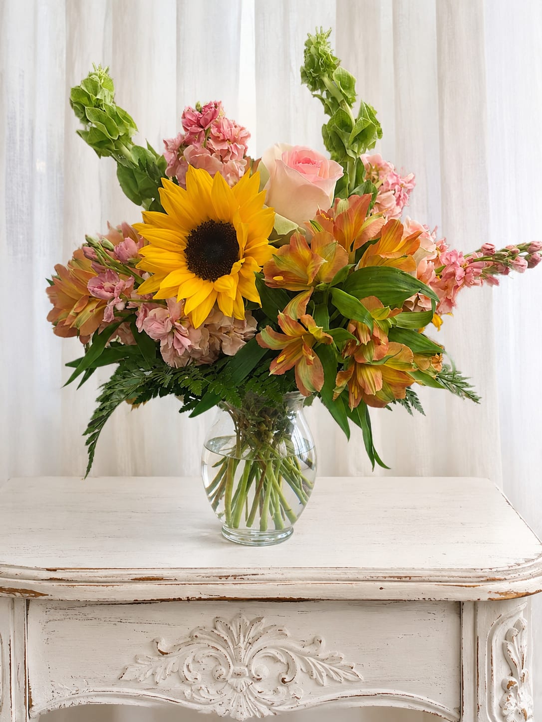 Bouquet of sunflowers, pink roses, and mixed blooms in a clear glass vase