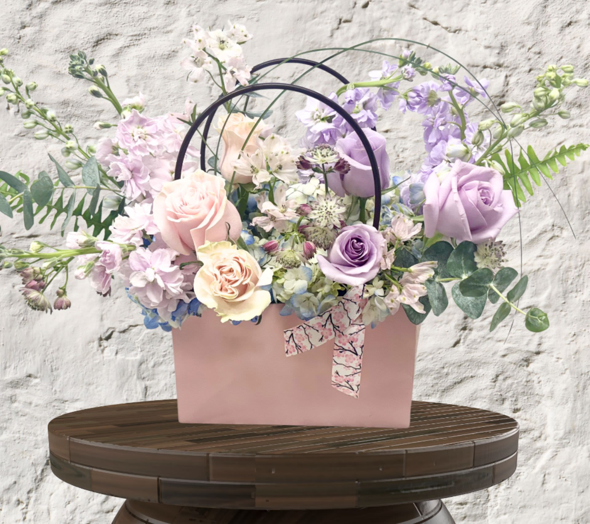 Artisan Blooms Bag - "Hand-crafted by accredited Master Florist Tricia Won (AIFD, EMC, IMF) using premium seasonal market blooms. No two arrangements are identical."  Redefine the floral experience with our Artisan Bloom Bag—the ultimate fusion of premium floristry and modern convenience. This is a fully designed floral moment housed in a signature, upscale carry-tote with sleek handles and a tailored ribbon finish. Designed for the modern romantic, it is easy to carry and ready to be displayed as a chic, self-contained piece of decor.  Each Bloom Bag is a unique "Designer’s Choice" reflection of the week’s most exquisite harvest. Depending on our current curation, your bag will feature:  Vibrant &amp; Bold: Rich crimsons and jewel tones.  Soft &amp; Romantic: Pastels and ruffled textures.  Premium Accents: Finished with waxflowers, eucalyptus, or seasonal greenery for a lush, garden-inspired look.  Select Your Tier of Opulence The Petite Bloom Bag (Standard): A refined and charming gesture. Features a curated selection of premium focal roses and seasonal stock for a sophisticated "Petite Luxe" look.  The Deluxe Bloom Bag: Our most popular size. Significantly increases the stem count with high-end focal flowers like ruffled garden roses and exotic accents for an overflowing aesthetic.  The Premium Bloom Bag: The ultimate expression of luxury. Utilizes our rarest global imports and the highest stem density to create a massive floral display for milestone celebrations.