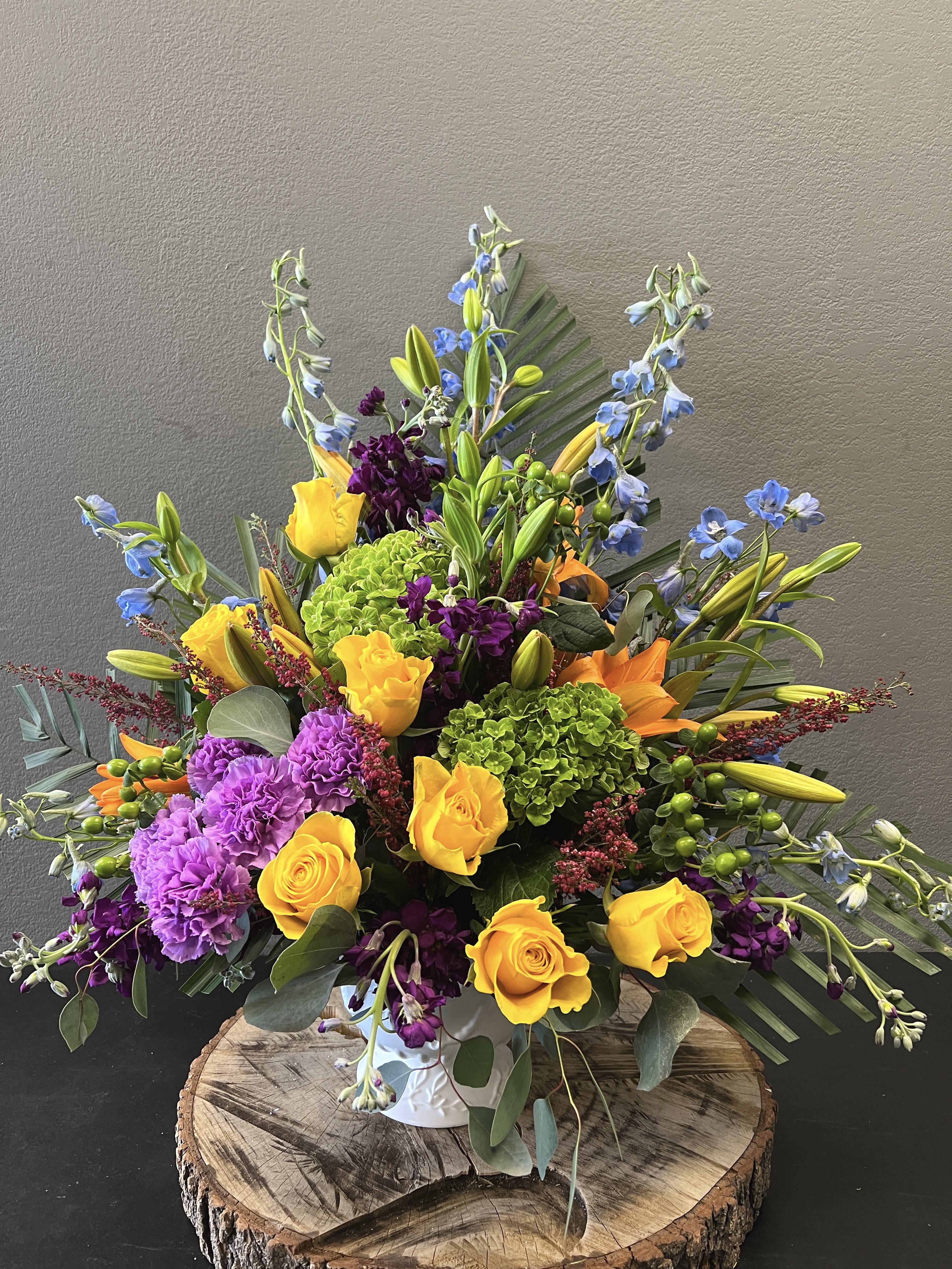 Bright mixed bouquet with yellow roses, purple carnations, and blue delphinium in a vase