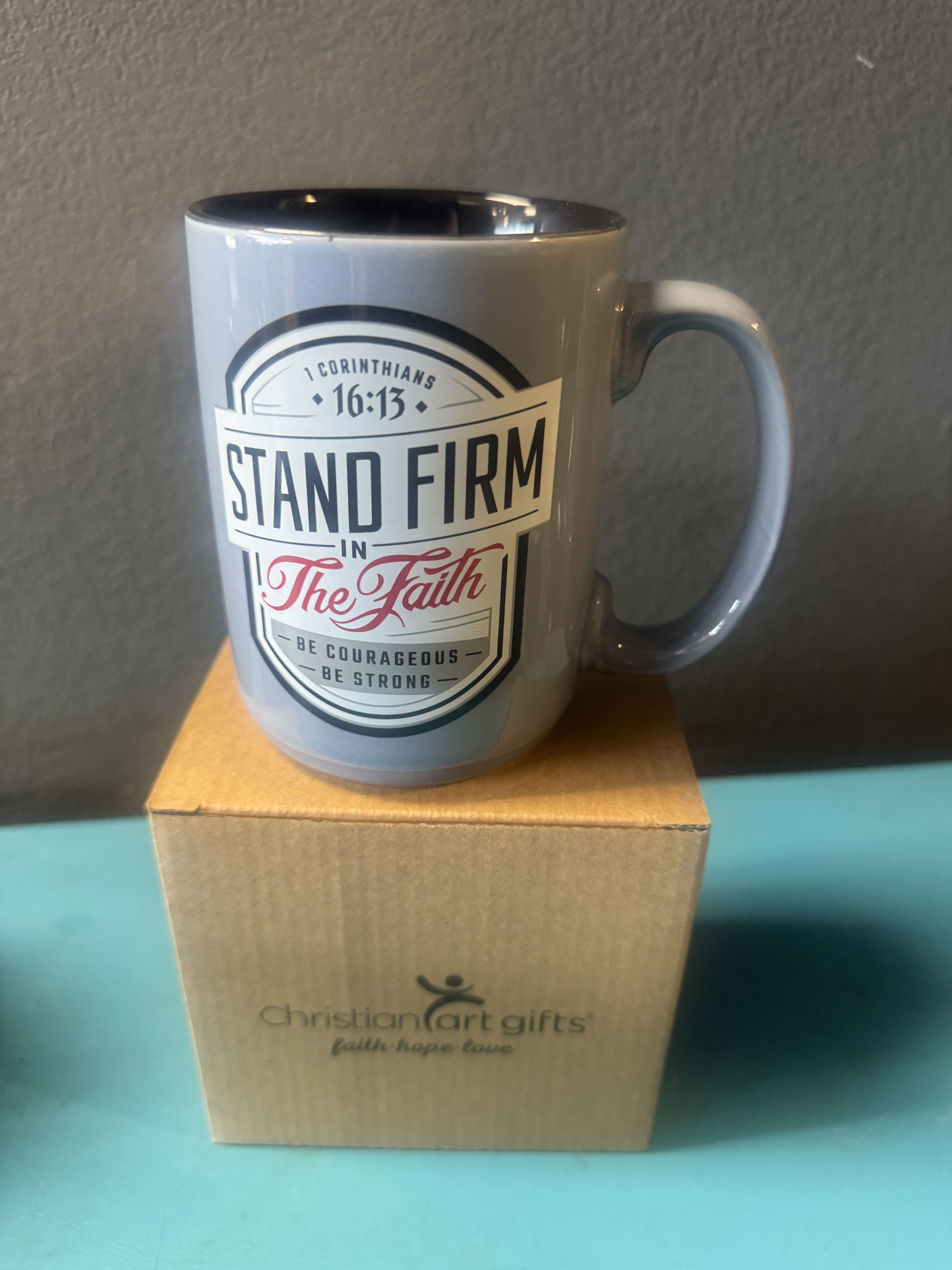 Gray mug with a faith message sitting on a cardboard box